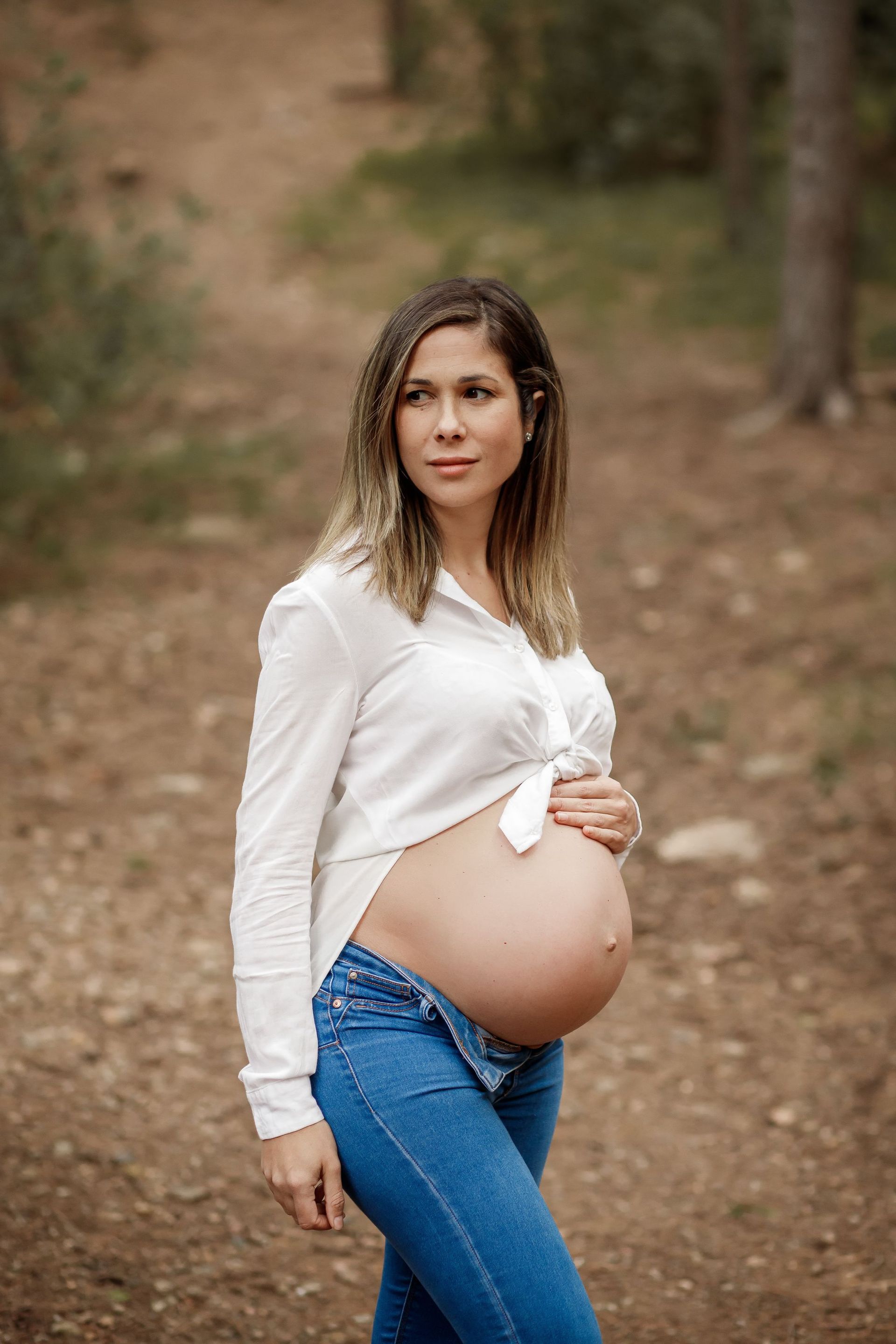 Una mujer embarazada está parada en el bosque sosteniendo su vientre.