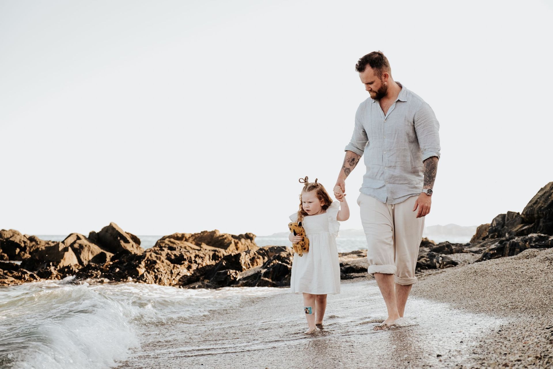 Un hombre y una niña caminan por la playa tomados de la mano.