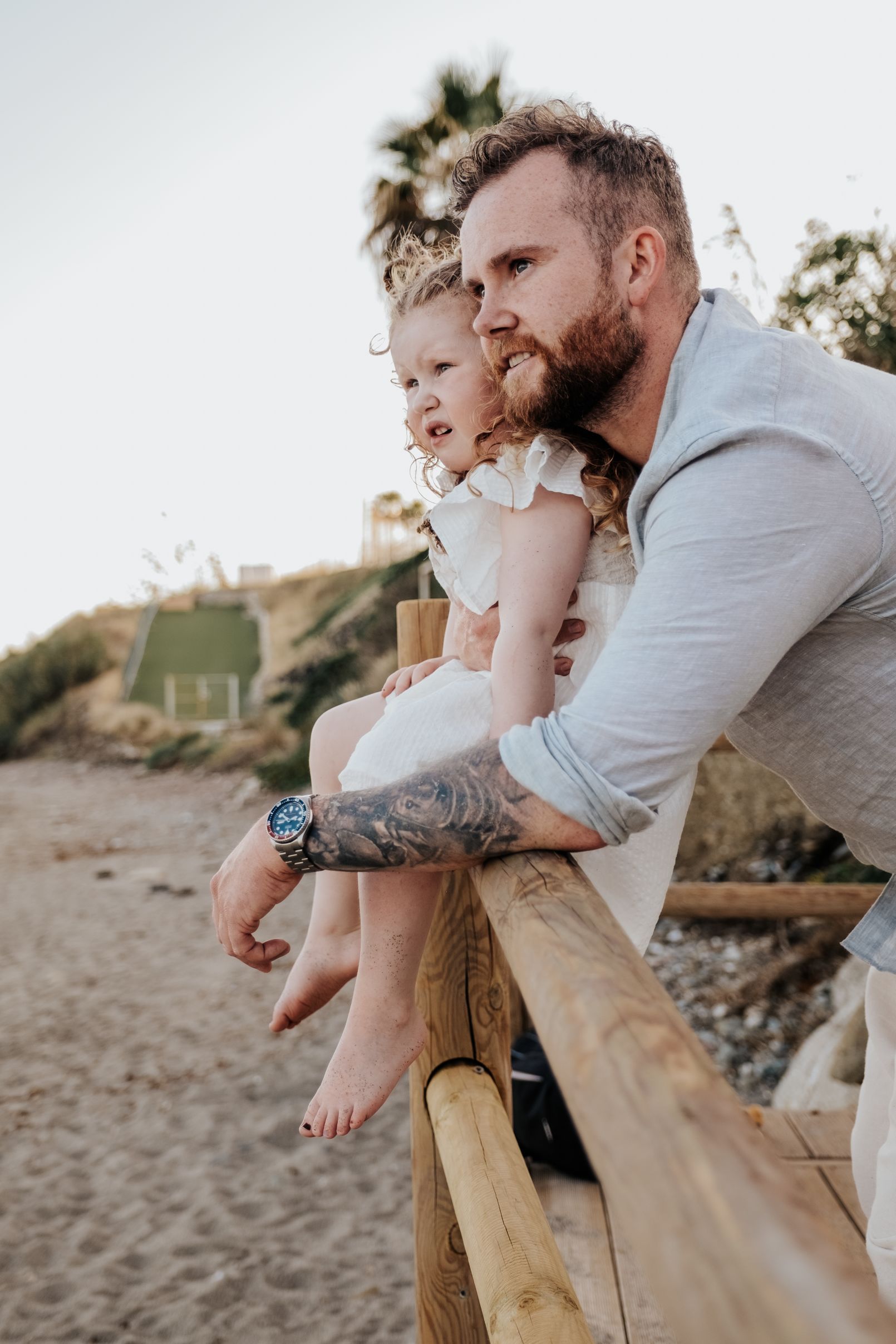 Un hombre y una niña están sentados en una barandilla de madera en la playa.