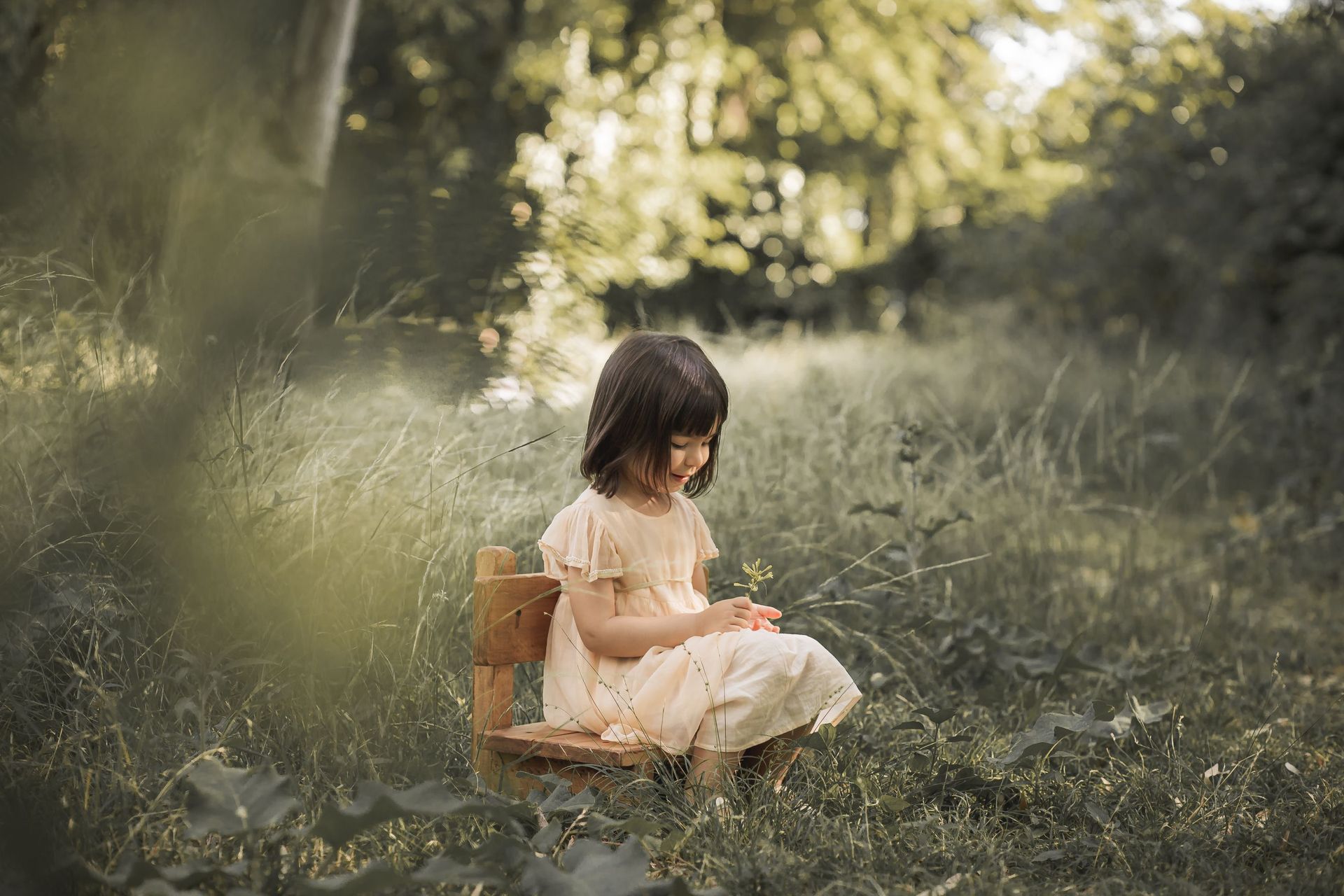 Una niña está sentada en una silla de madera en la hierba.