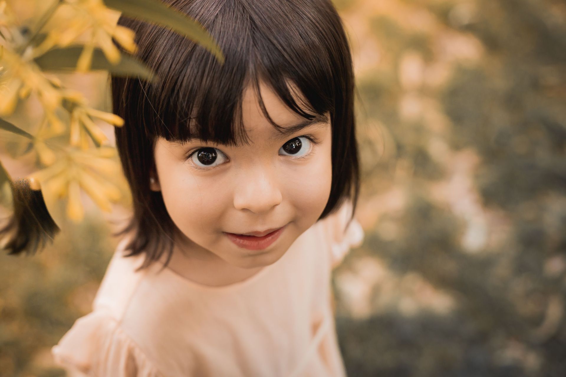 Una niña está parada frente a un árbol y mira a la cámara.