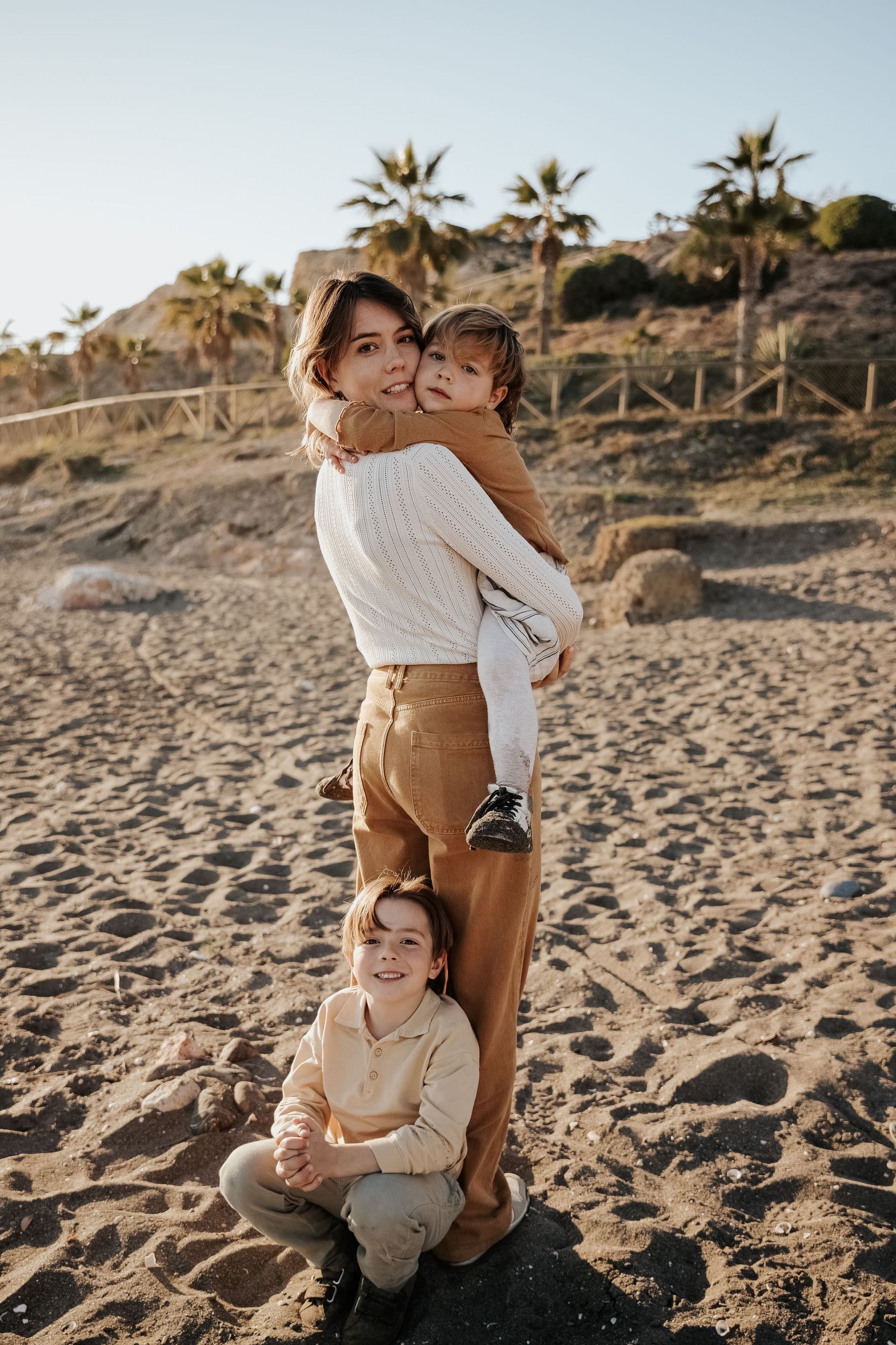 Una mujer sostiene a dos niños en la playa.