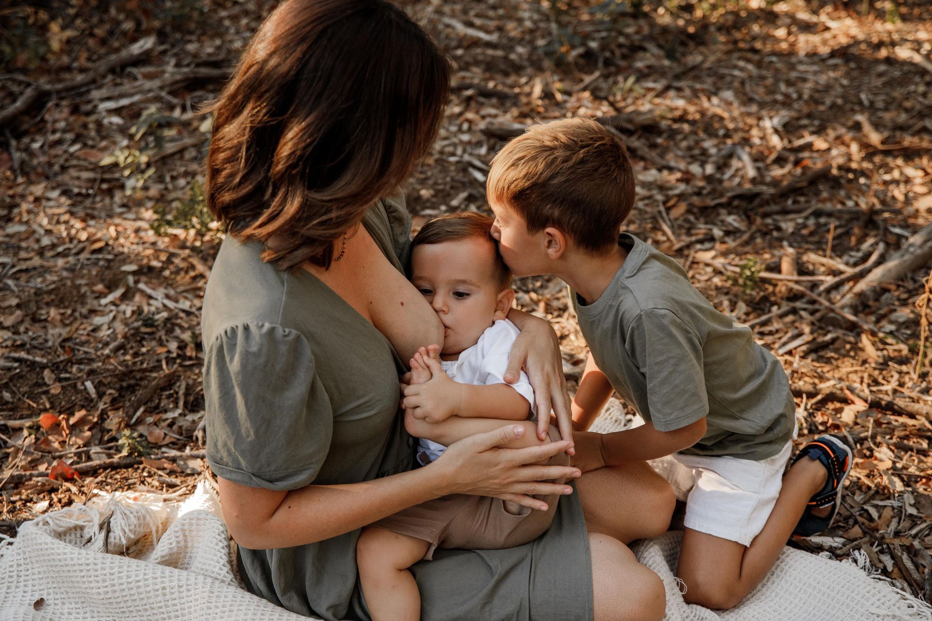 una mujer está amamantando a un bebé mientras dos niños la besan .