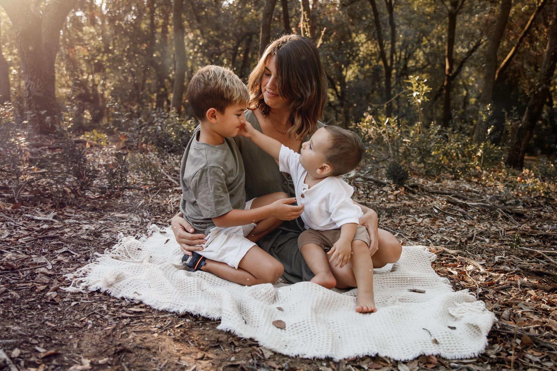 Una mujer está sentada en una manta con dos niños en el bosque.