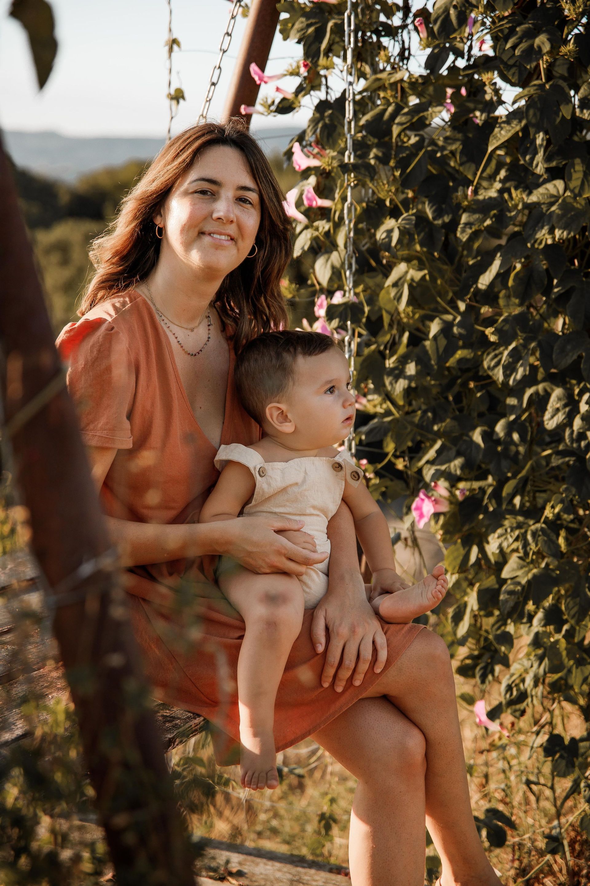 Una mujer está sentada en un columpio sosteniendo un bebé.