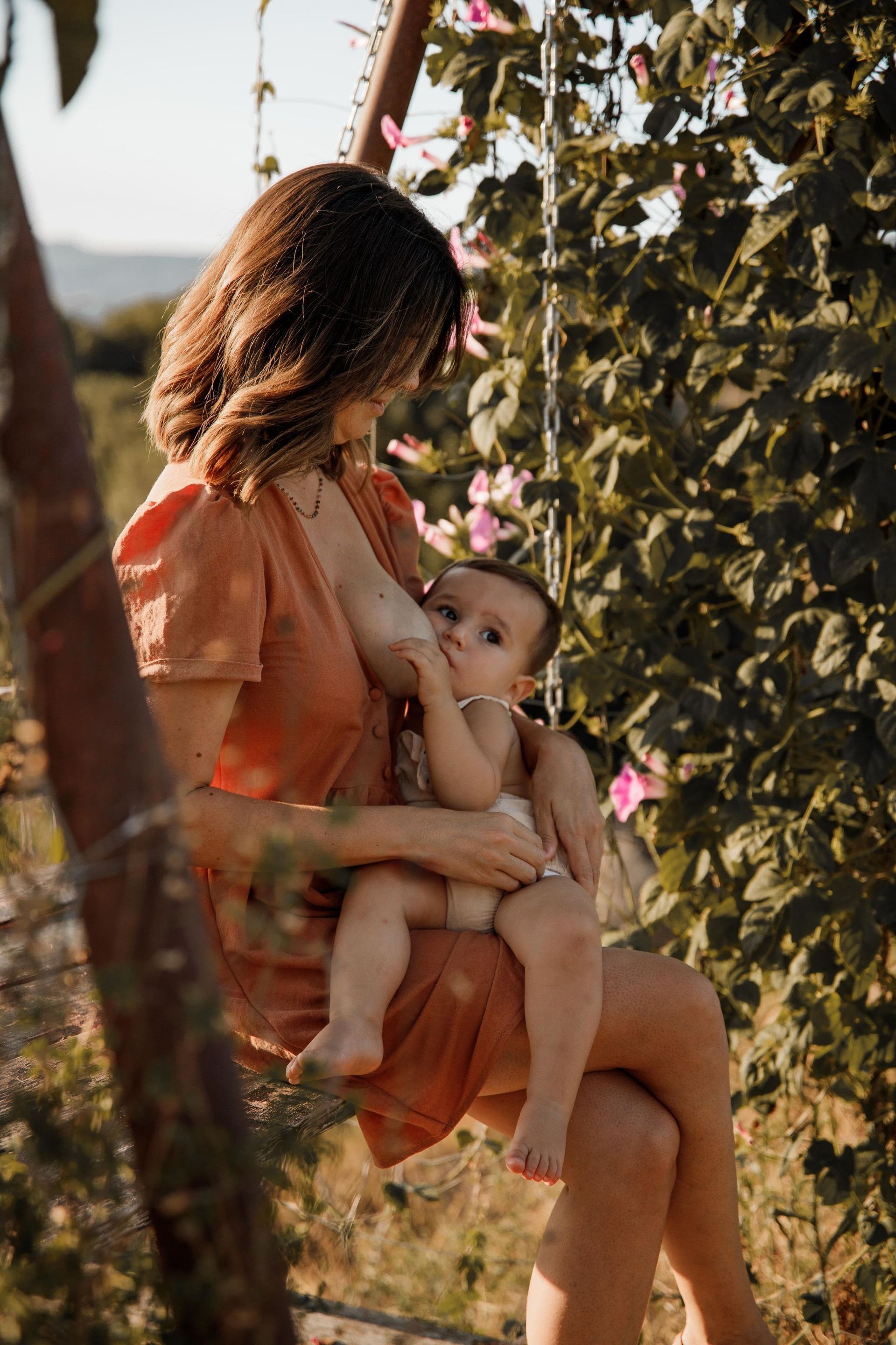 Una mujer está amamantando a su bebé mientras está sentada en un columpio en un campo.
