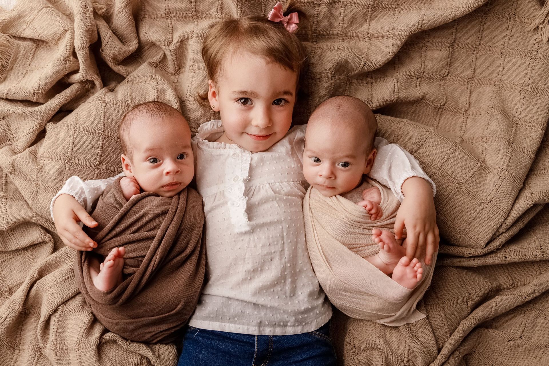 Una niña sostiene a dos bebés recién nacidos envueltos en mantas.