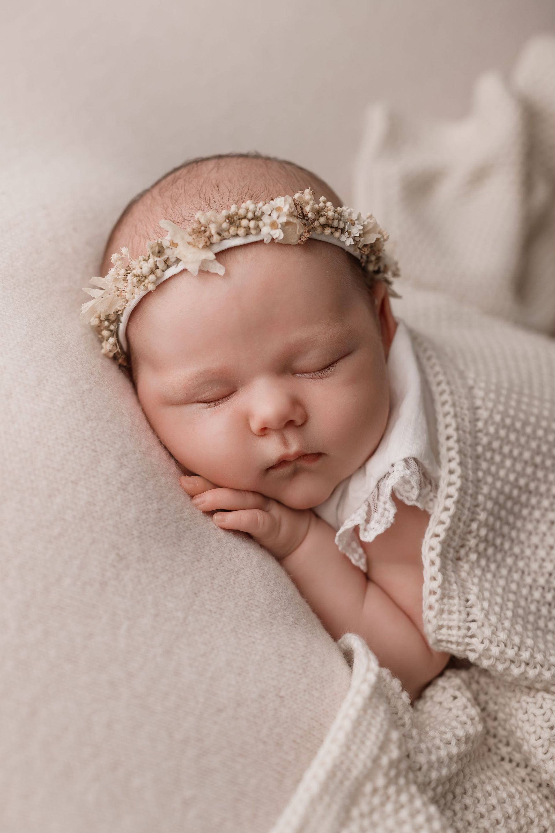 Un bebé recién nacido que lleva una diadema de flores está durmiendo sobre una manta.