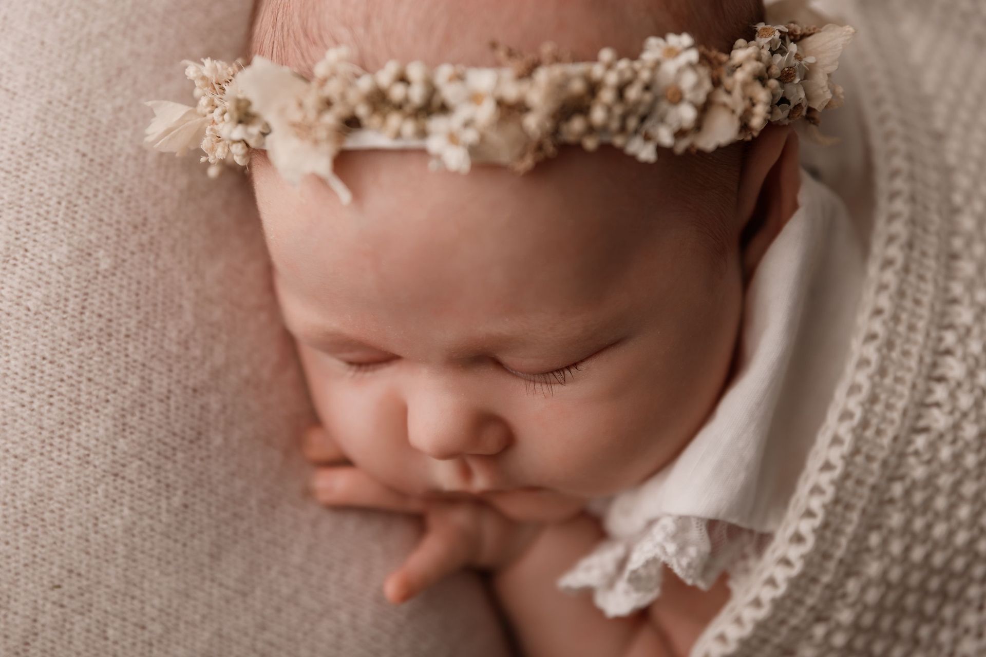 Un bebé recién nacido que lleva una corona de flores está durmiendo sobre una manta.