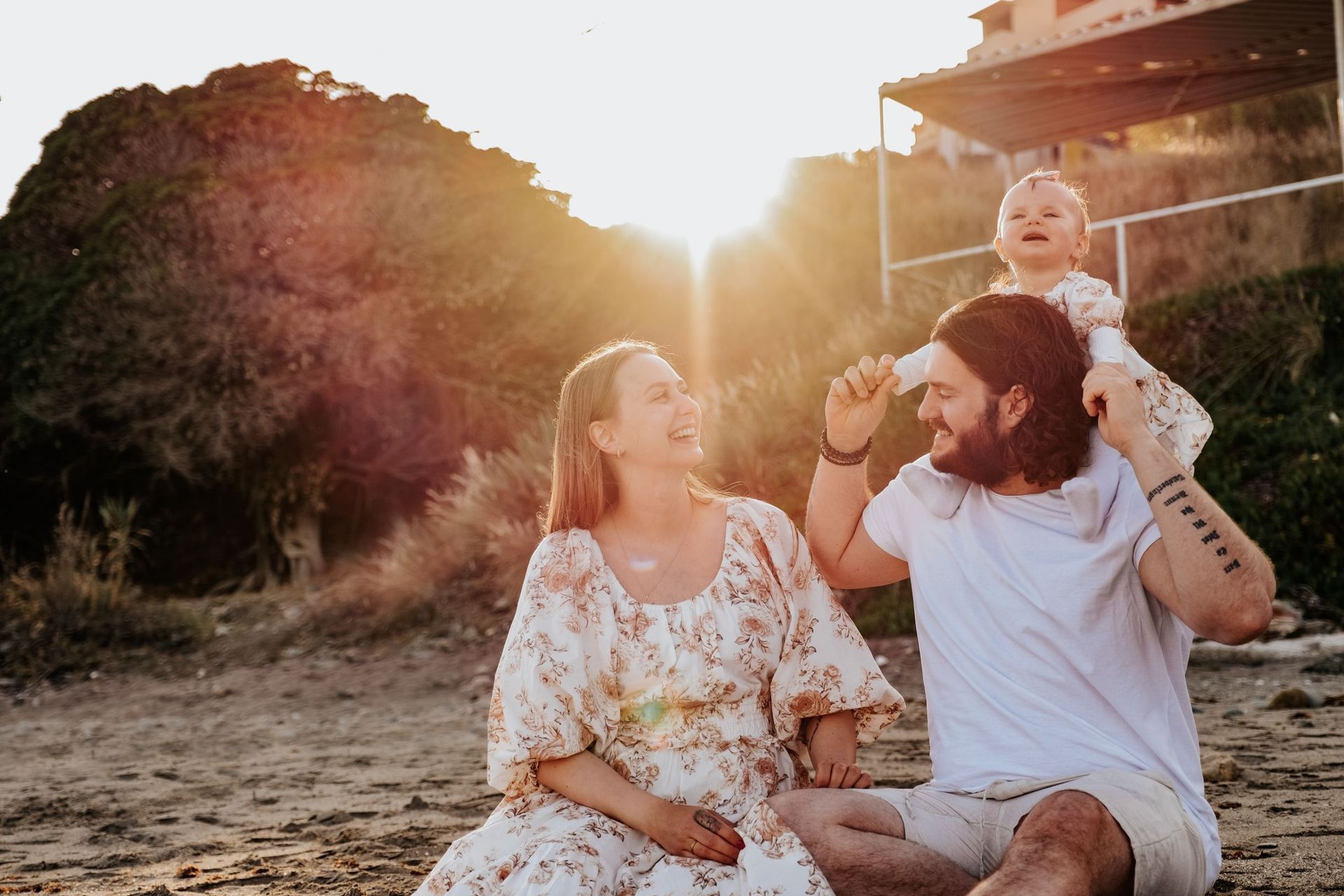 Un hombre y una mujer están sentados en la playa sosteniendo un bebé.