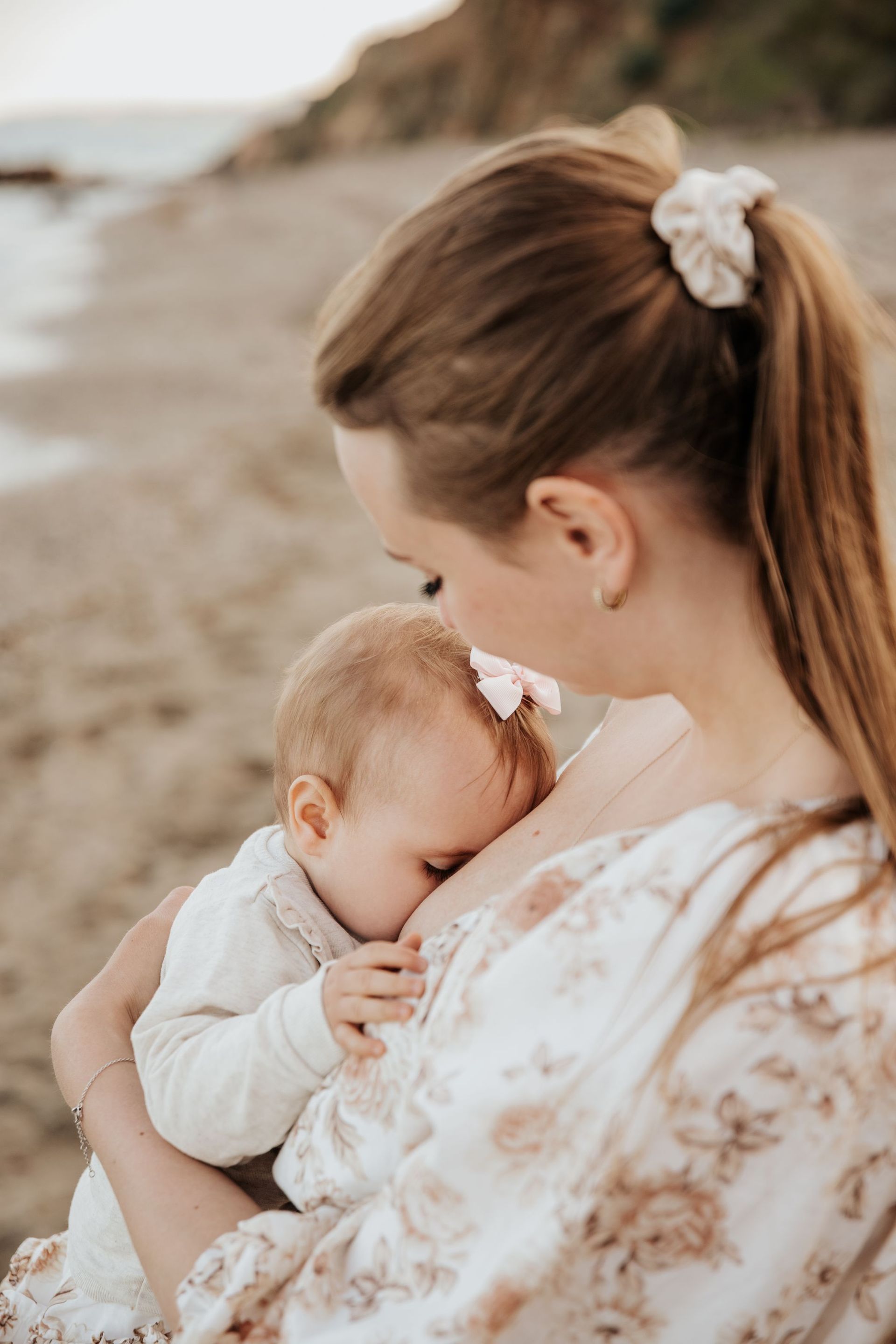 Una mujer está amamantando a su bebé en la playa.