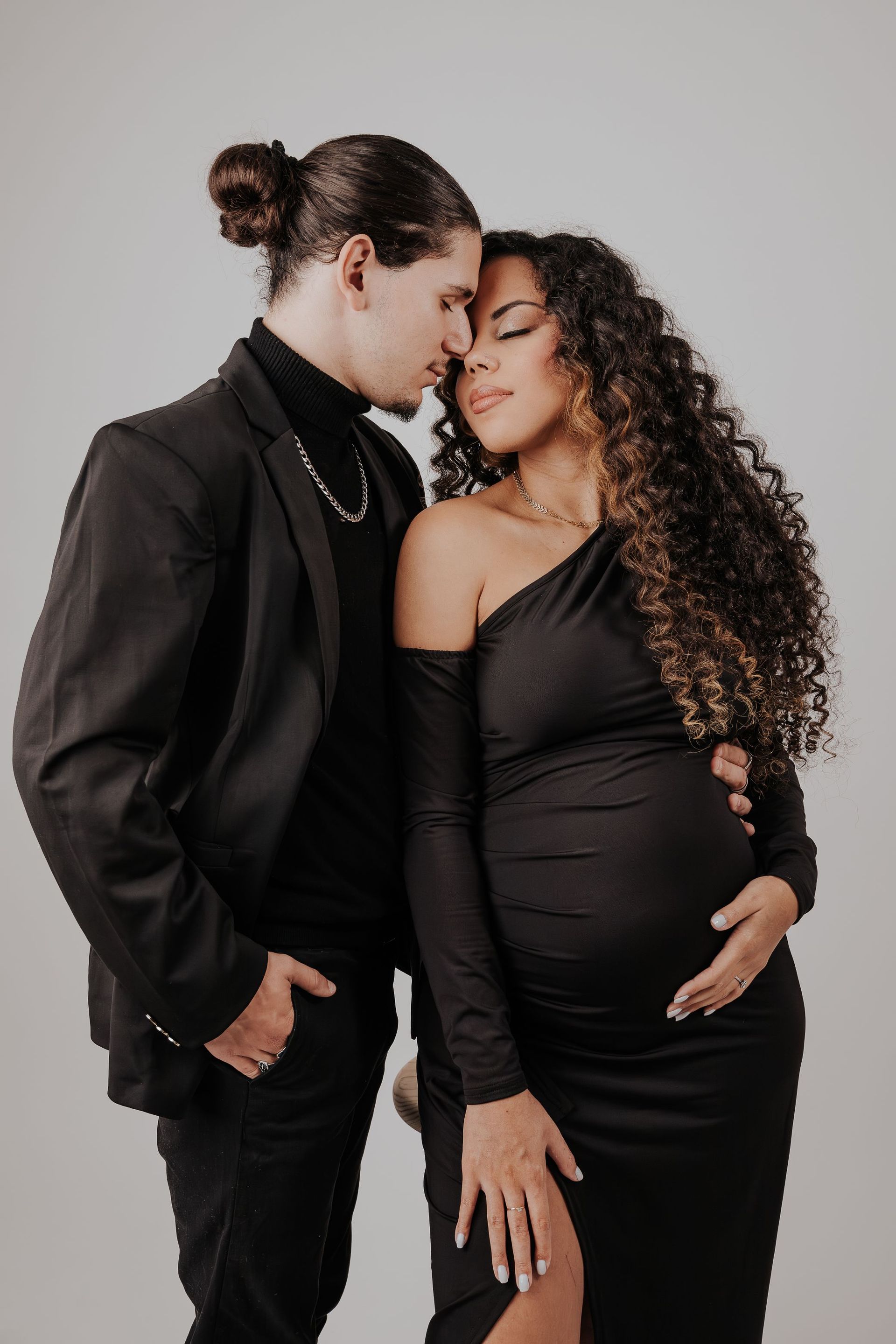 Una mujer embarazada con un vestido negro está de pie junto a un hombre con traje.
