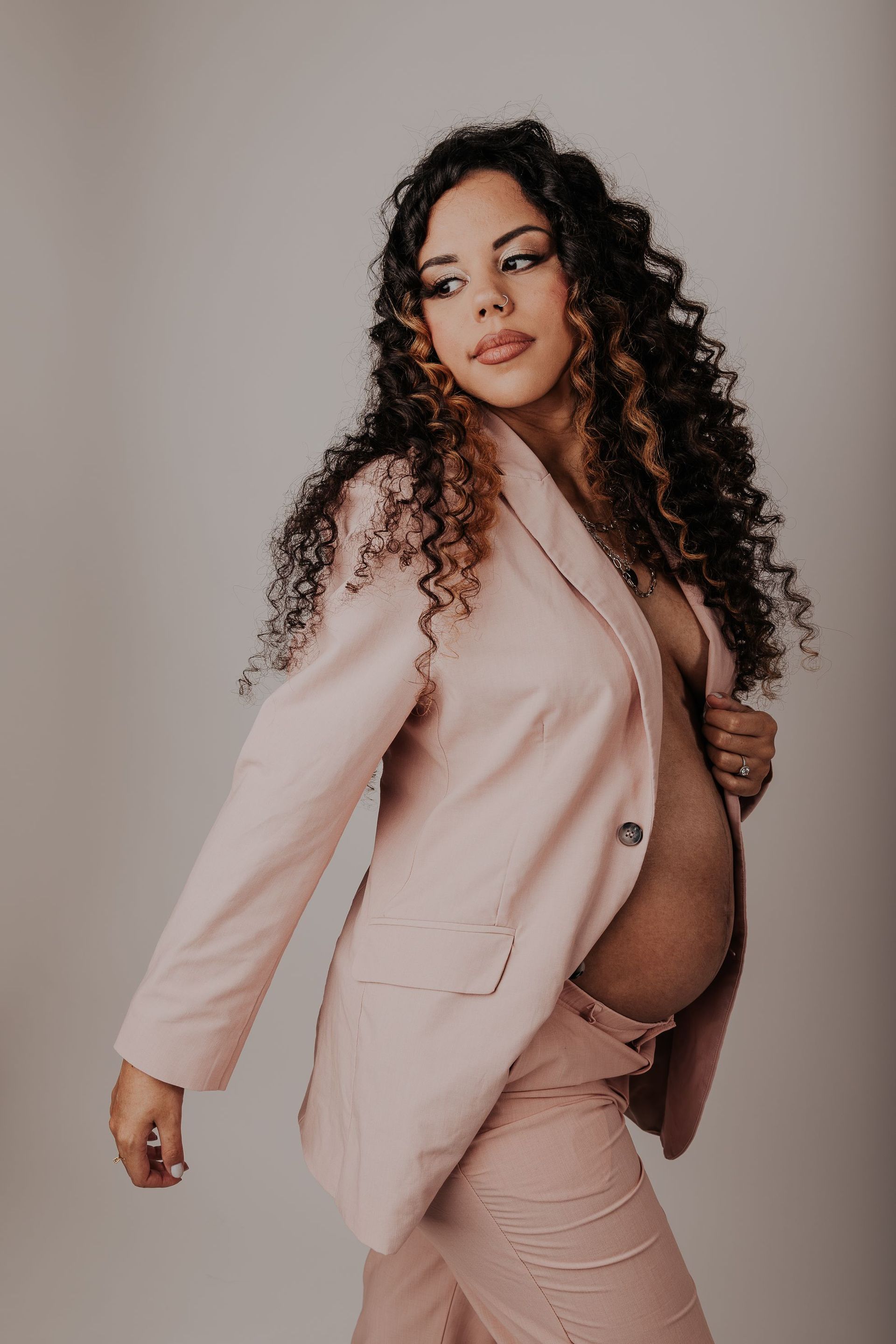 Una mujer embarazada lleva una chaqueta y pantalones de traje de color rosa.