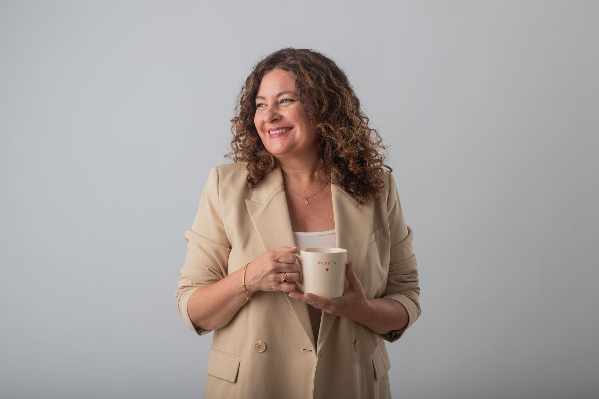 Una mujer con una chaqueta color canela sostiene una taza de café.