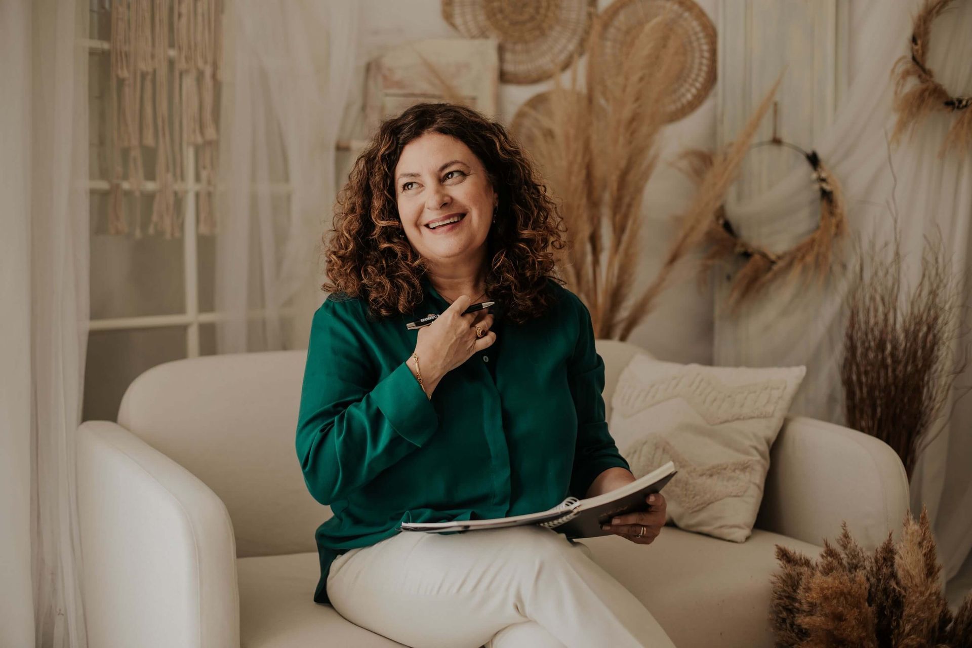 Una mujer está sentada en un sofá sosteniendo un libro y sonriendo.