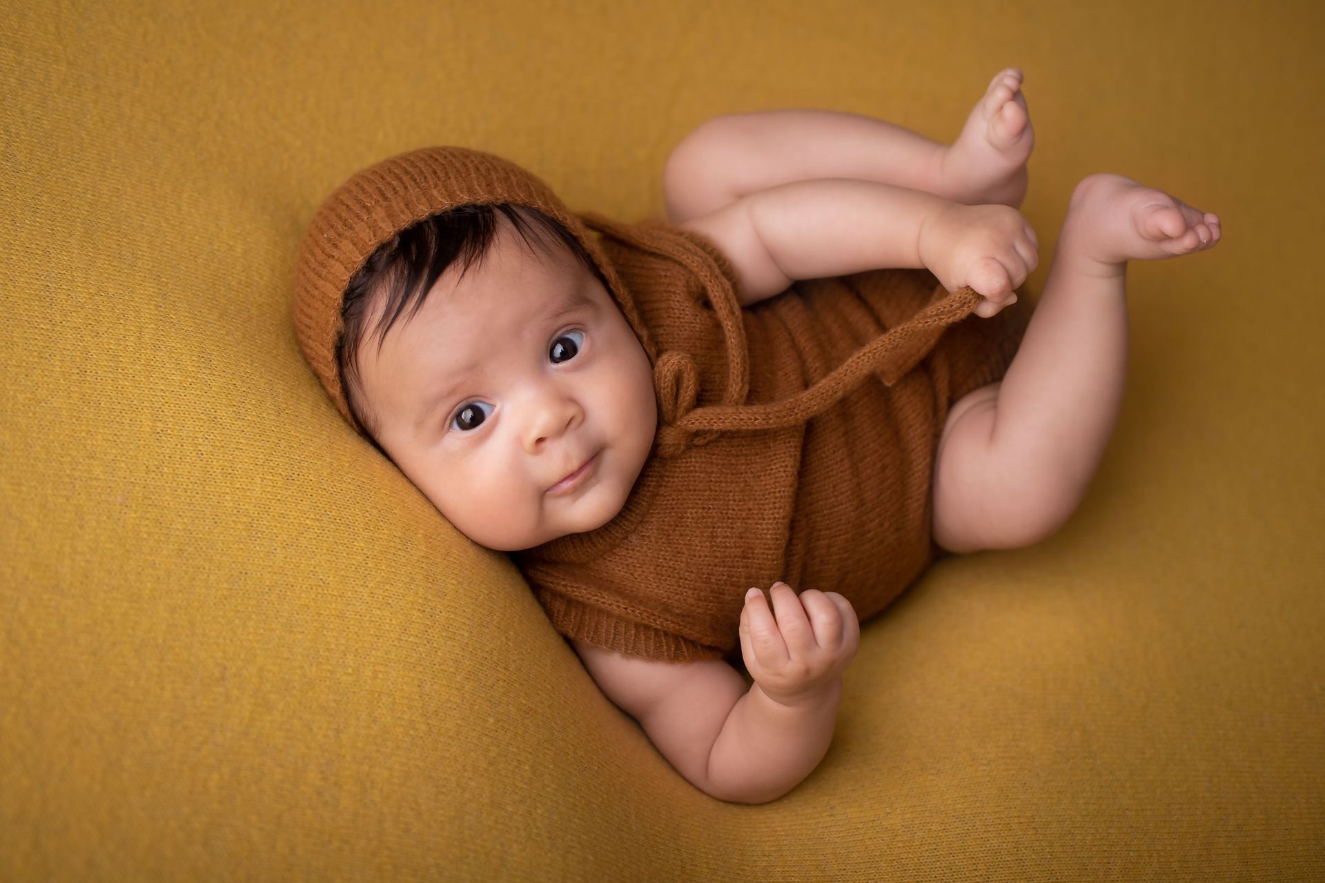 Un bebé con un traje marrón está acostado sobre una manta amarilla.