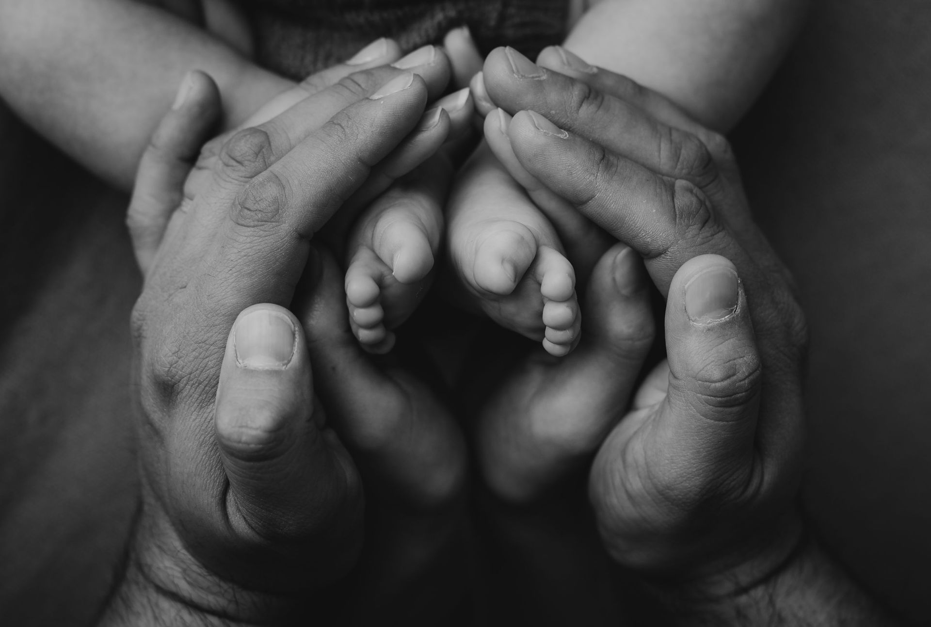 En una fotografía en blanco y negro, un hombre sostiene los pies de un bebé en sus manos.