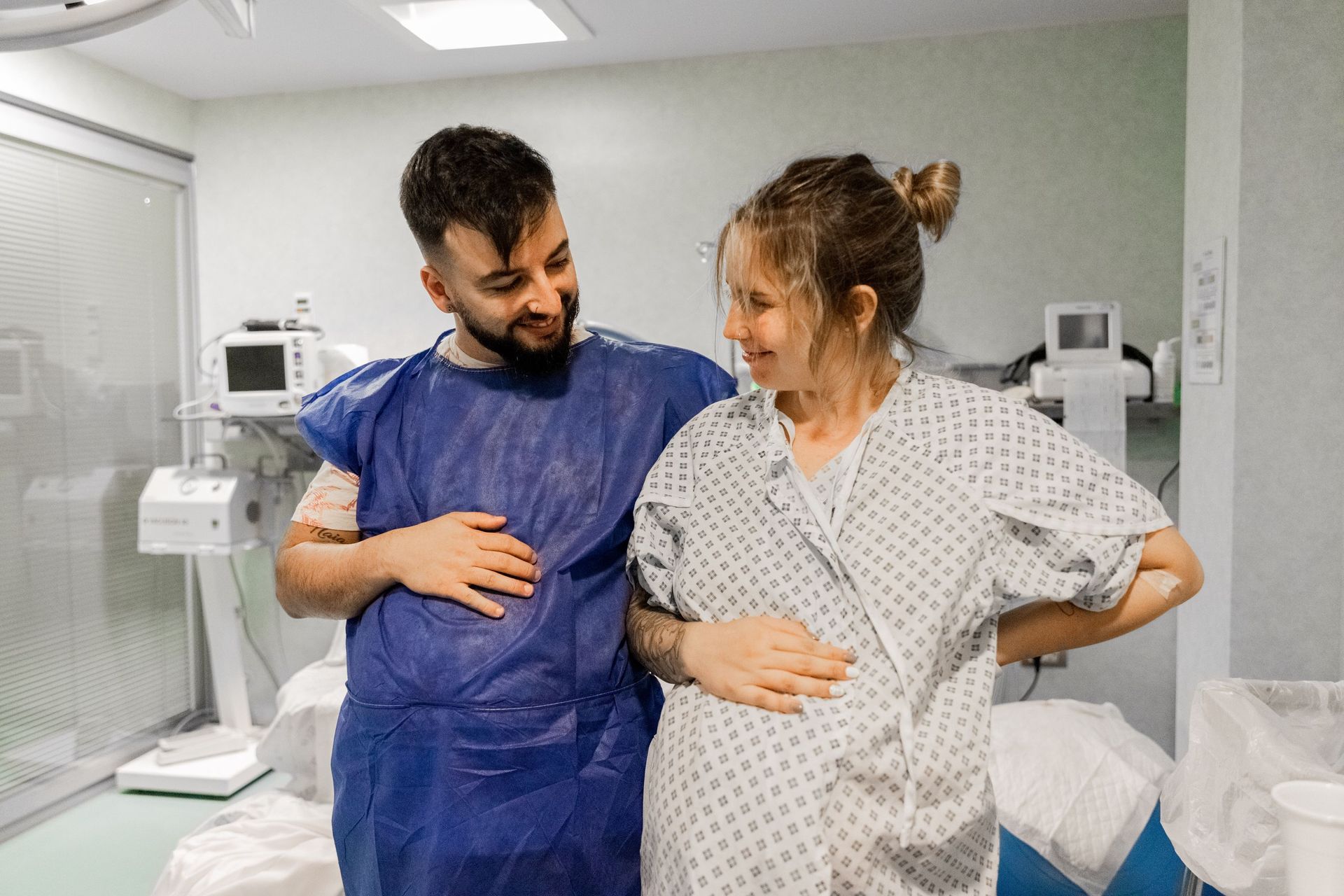 Un hombre y una mujer embarazada están parados uno al lado del otro en una habitación de hospital.
