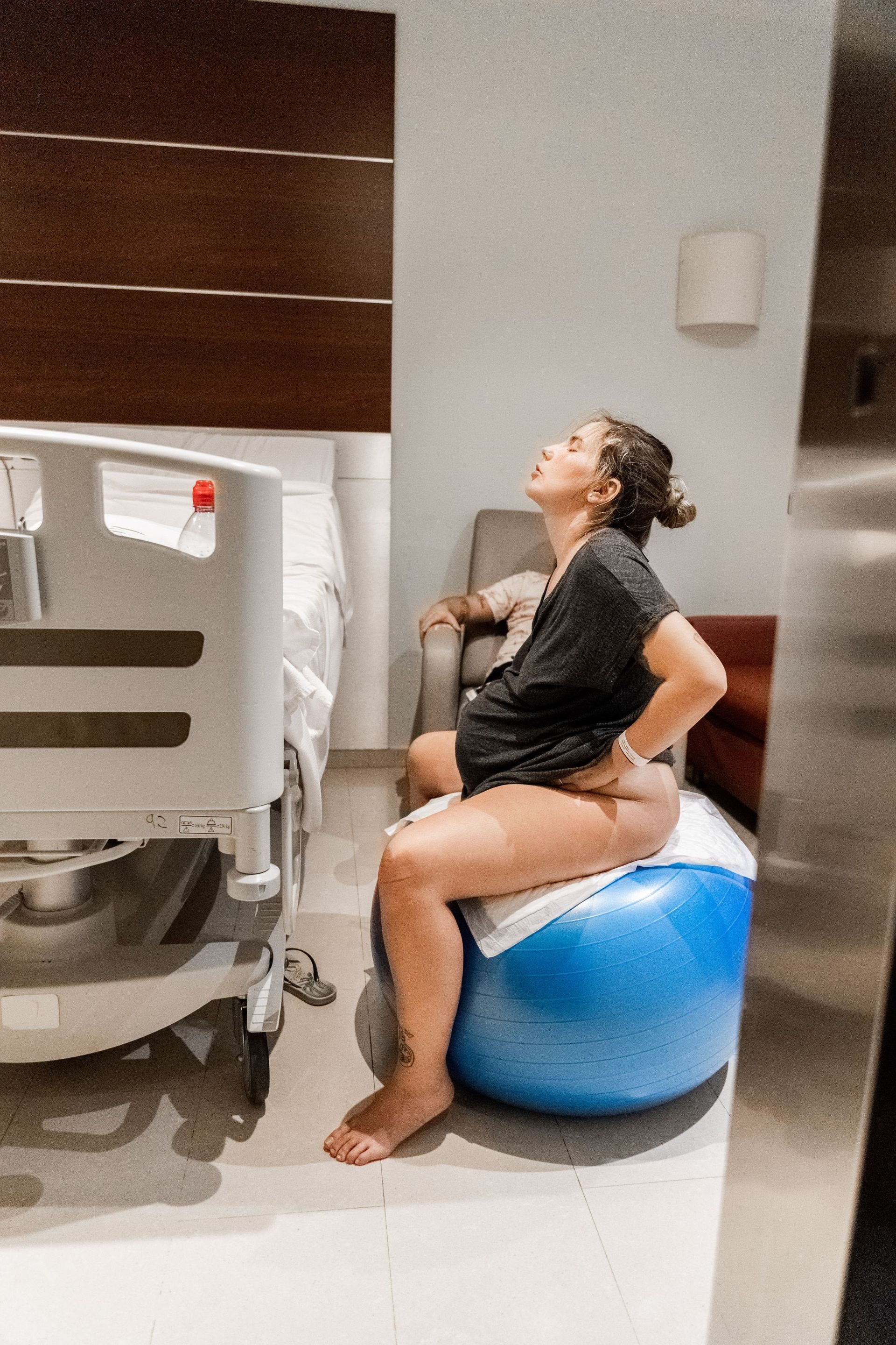 Una mujer embarazada está sentada sobre una pelota de ejercicio azul en una habitación de hospital.