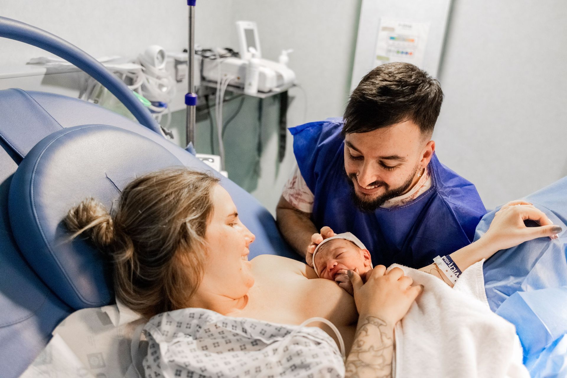 Un hombre y una mujer sostienen a un bebé recién nacido en una cama de hospital.