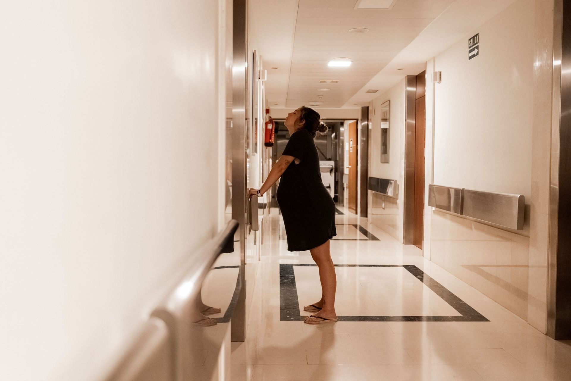 Una mujer embarazada está parada en el pasillo de un hospital mirando hacia arriba.