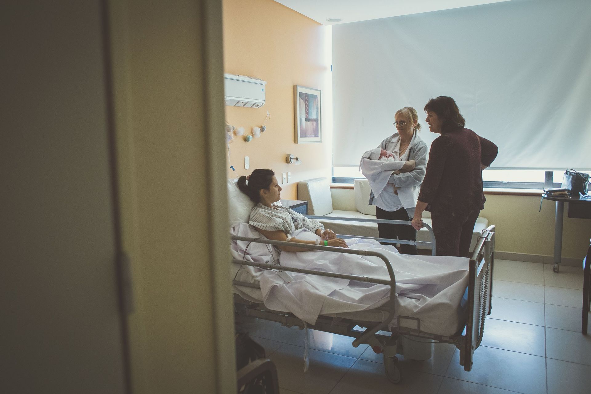 Una mujer está acostada en una cama de hospital con dos mujeres de pie a su alrededor.