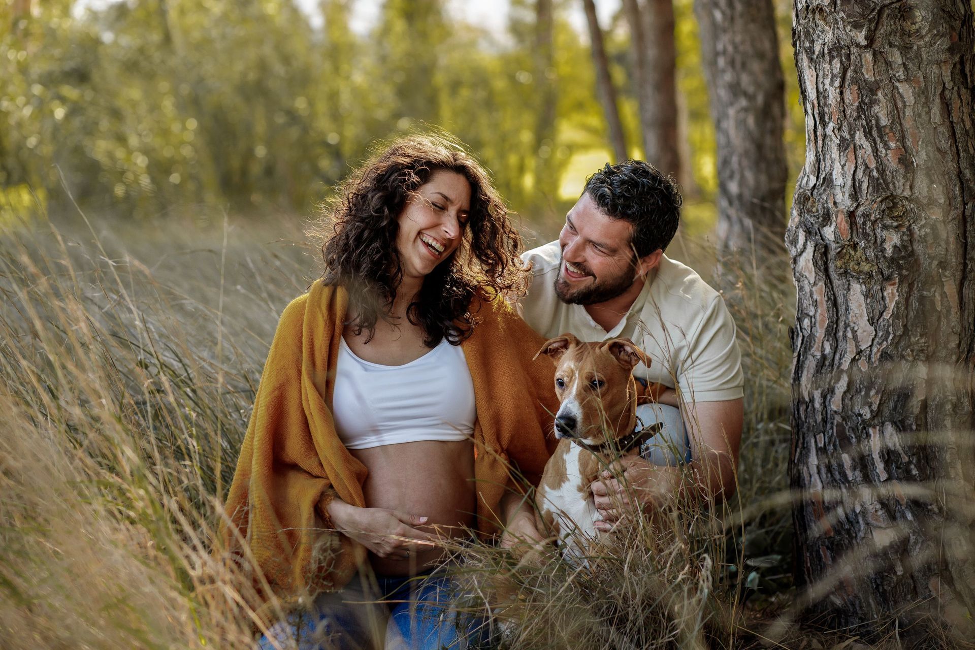 Una mujer embarazada y un hombre están sentados en un campo con un perro.