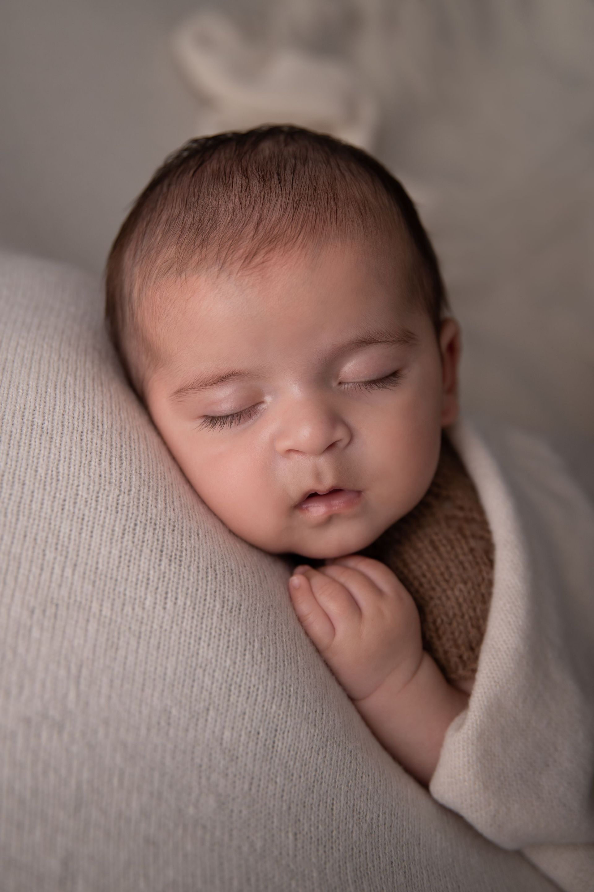Un bebé recién nacido envuelto en una manta blanca duerme sobre una almohada.