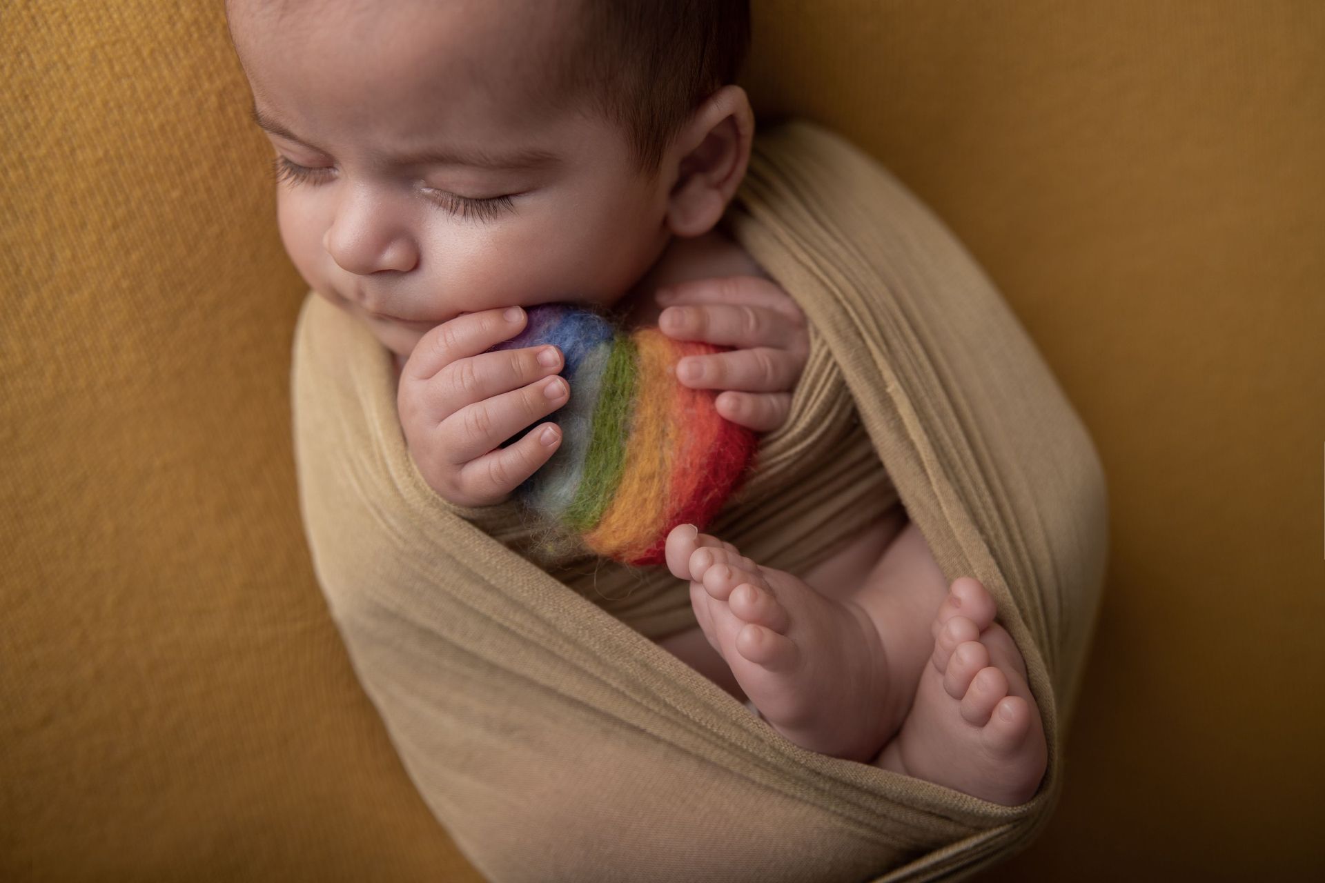Un bebé recién nacido está envuelto en una manta y sostiene un arco iris en su boca.