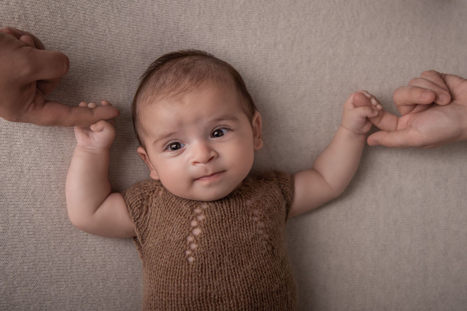 Un bebé está acostado sobre una manta con sus padres tomándole de la mano.