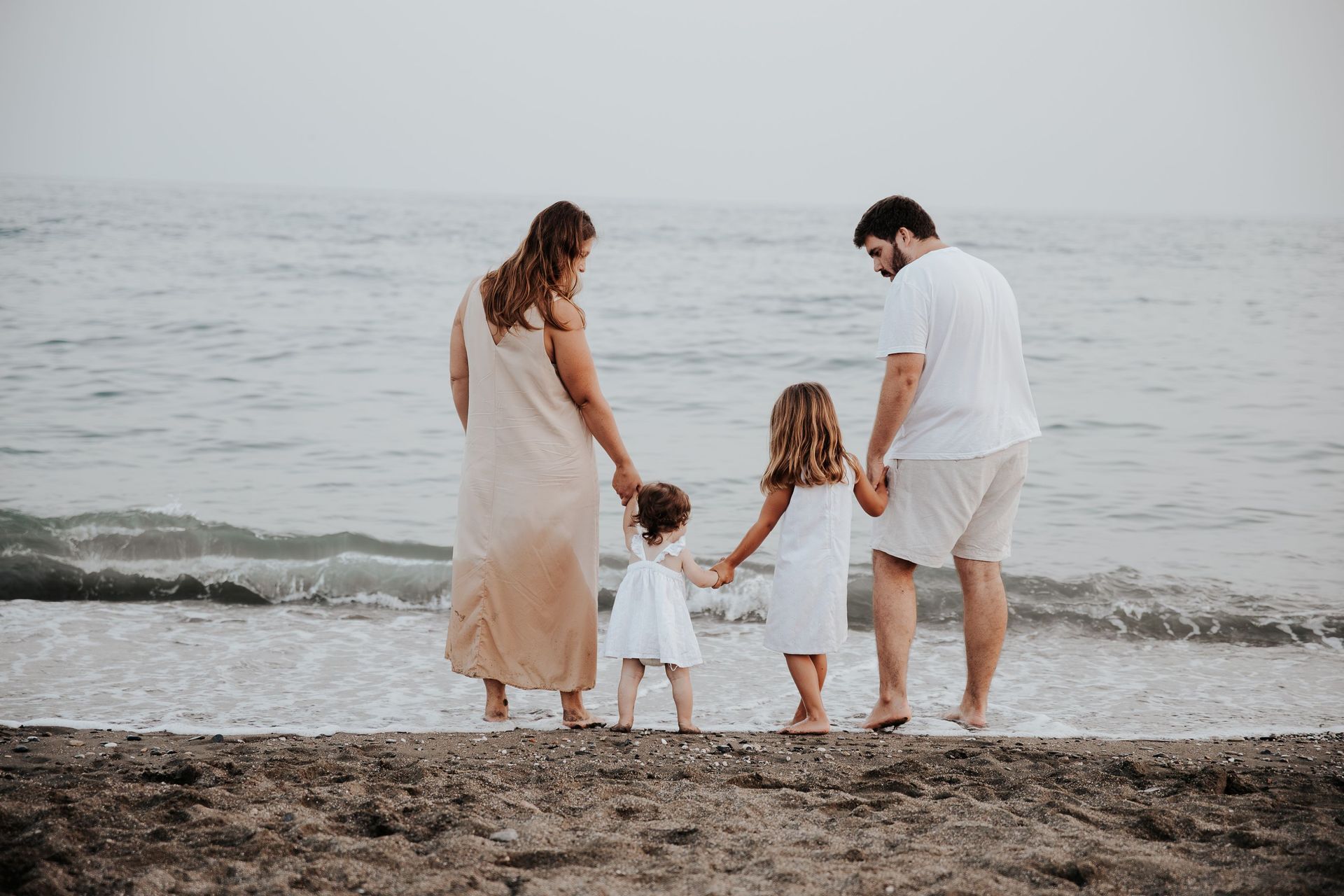 Una familia está parada en una playa tomada de la mano.
