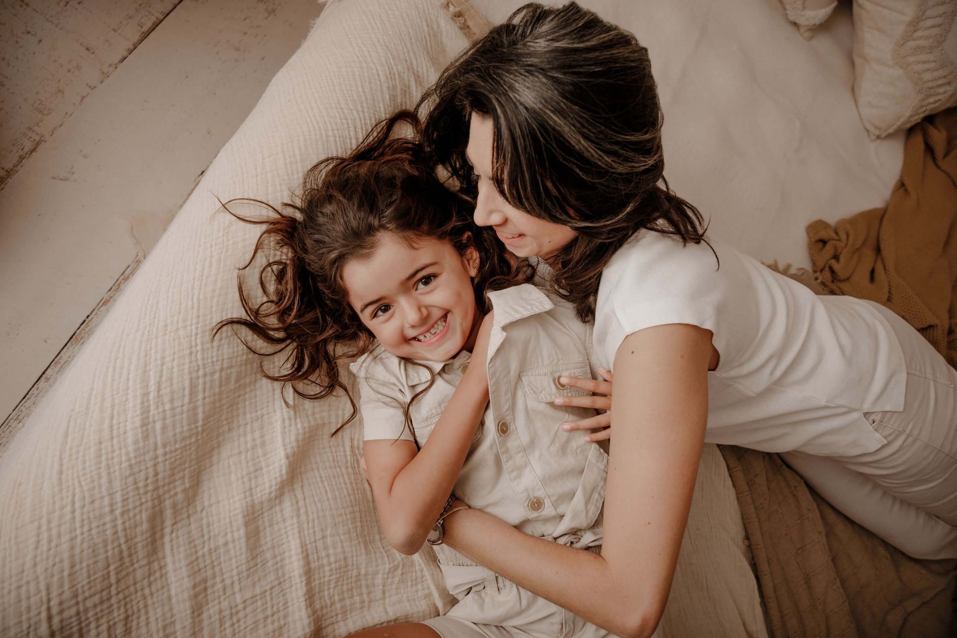 Una mujer abraza a un niño en una cama; ambos sonríen. Fotografía en tonos cálidos.