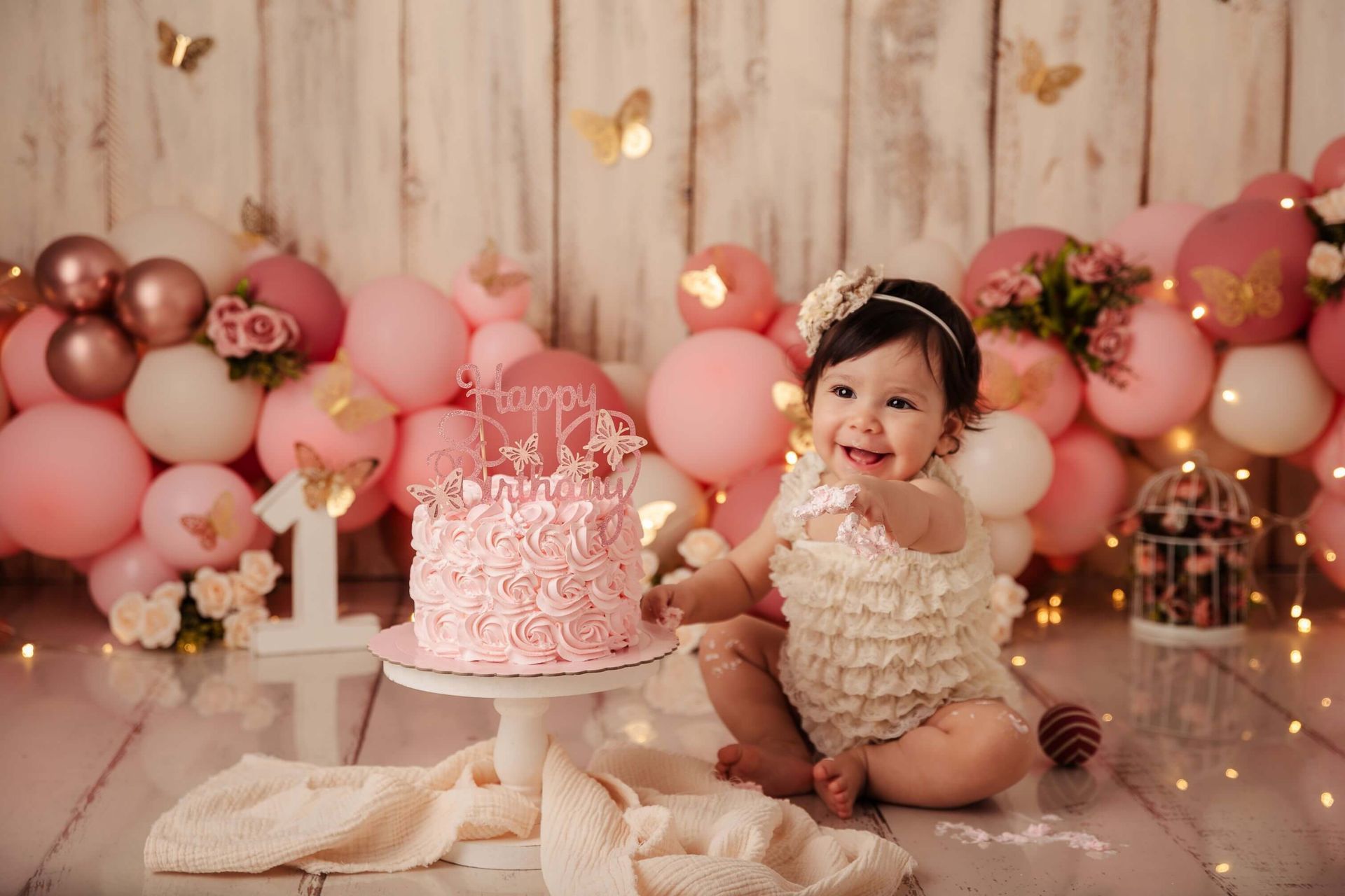 Una niña sonríe ante su primer pastel de cumpleaños, rodeada de globos rosas y mariposas en su reportaje Smash Cake en Málaga