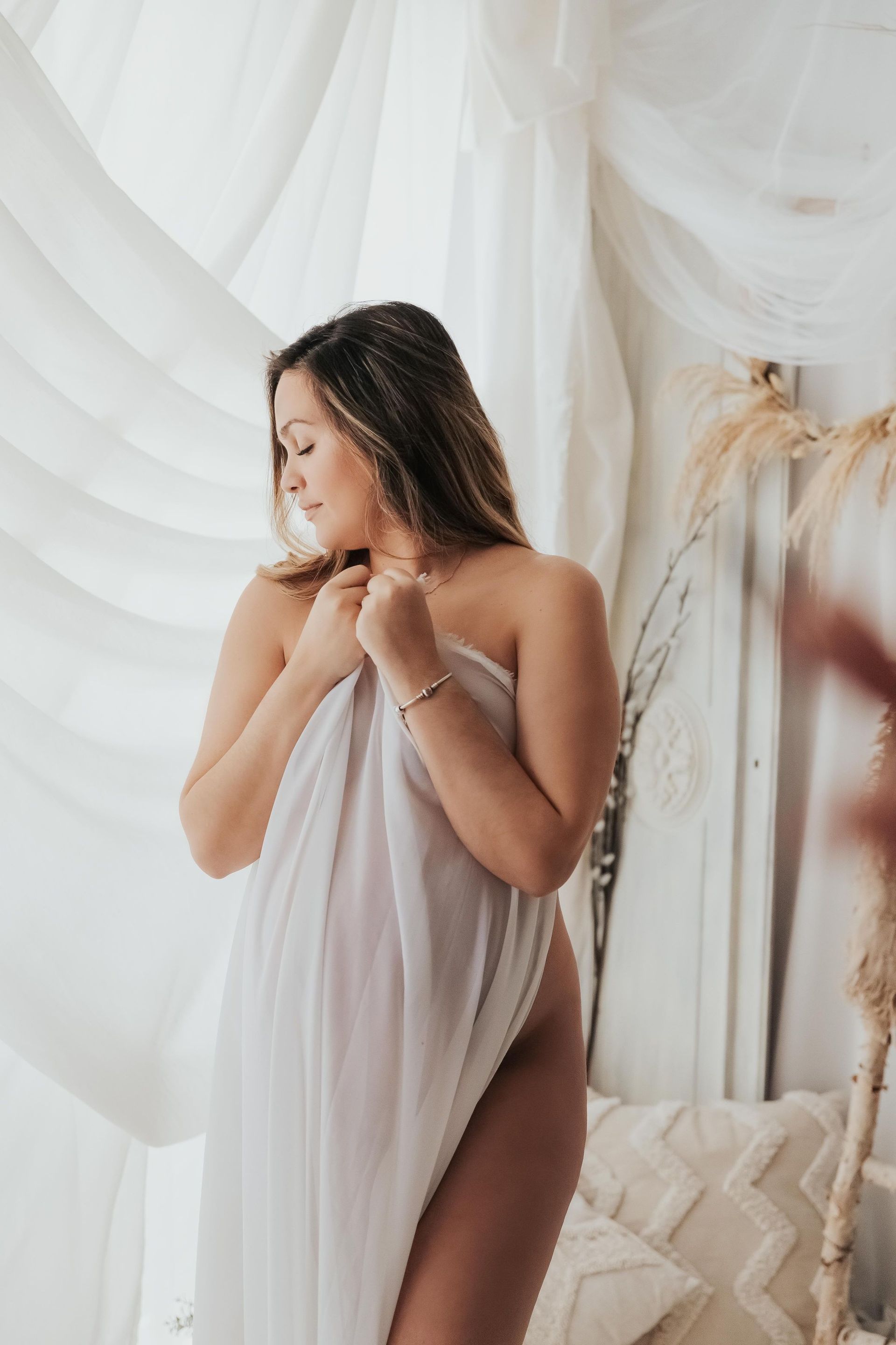 Una mujer envuelta en una tela blanca está parada frente a una ventana.