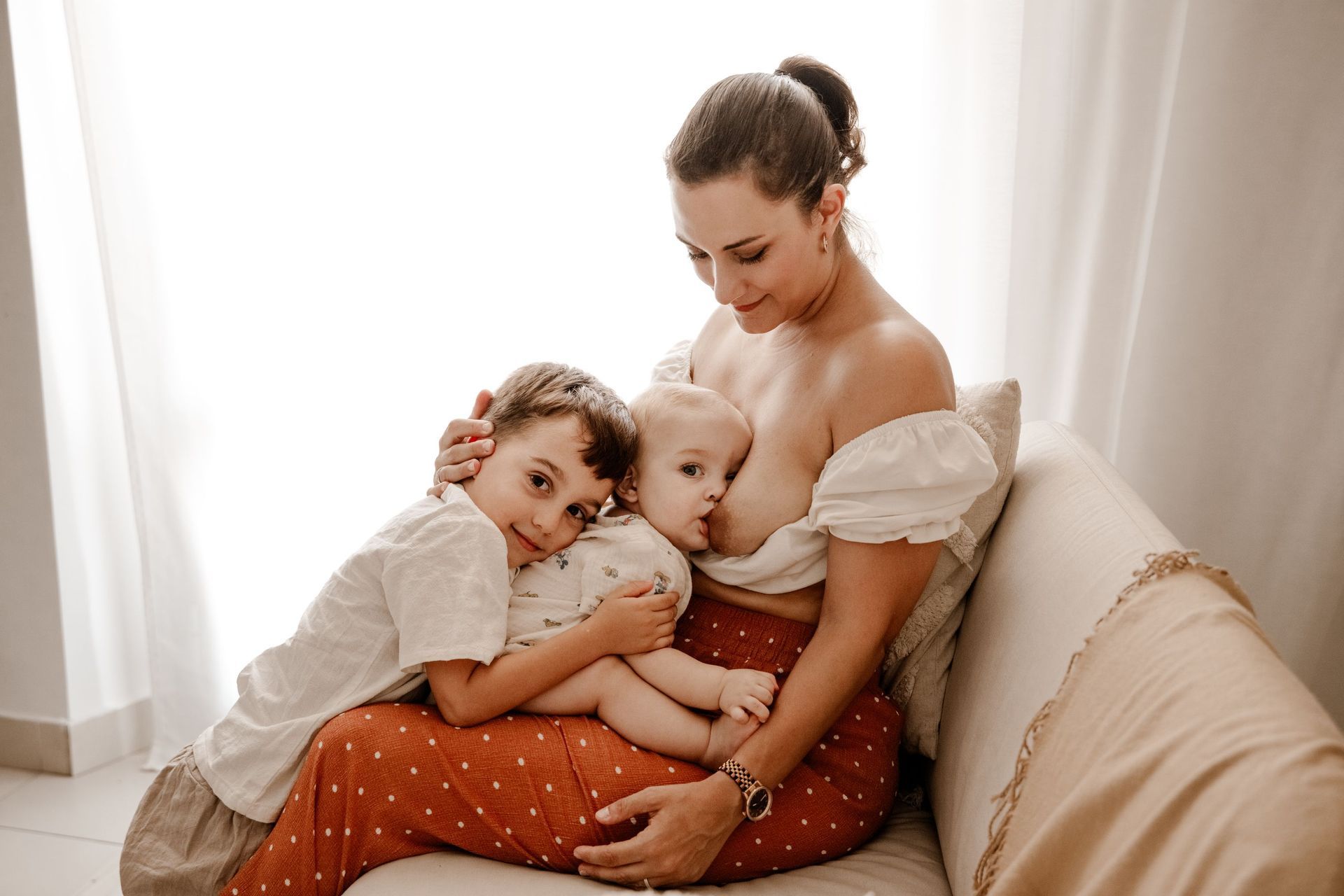 Una mujer está amamantando a dos niños en un sofá.