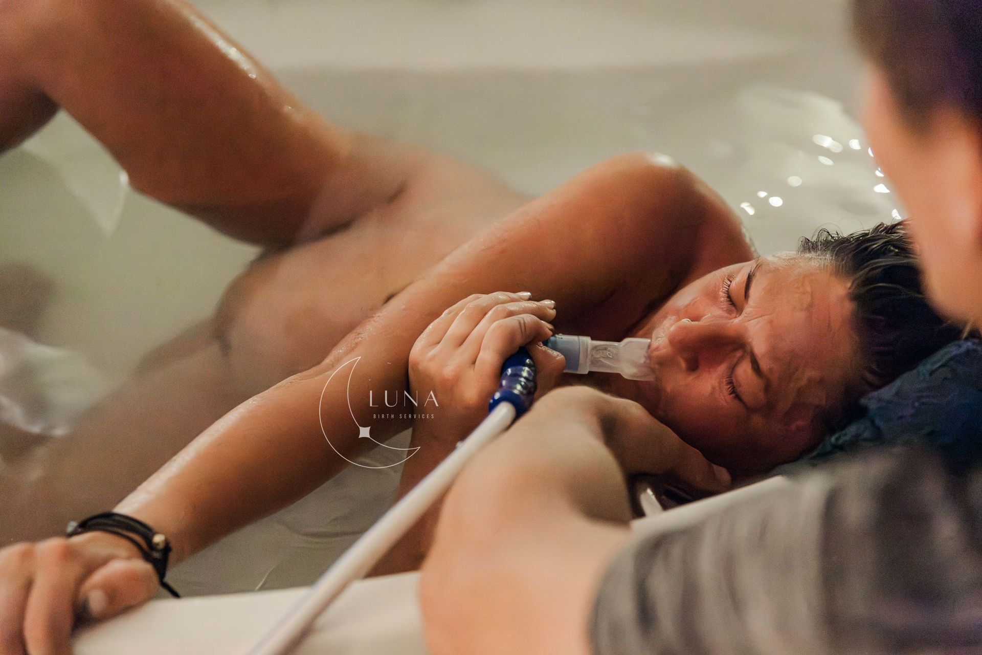 Mujer en una tina con agua, usando un respirador artificial durante el parto. Su pareja la sostiene.