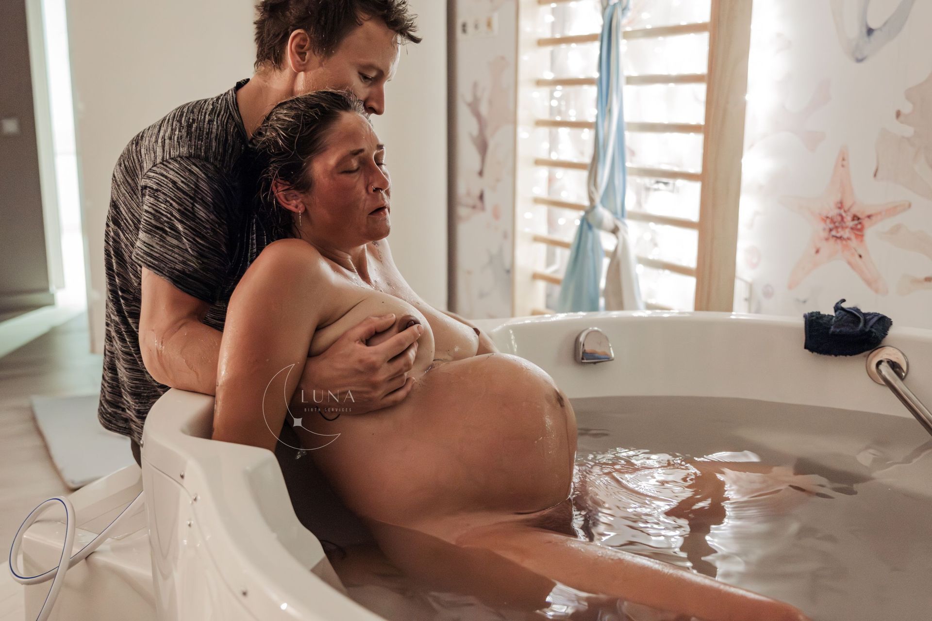 Embarazada en una bañera de parto con su pareja. Salpicaduras de agua. Se le ayuda a pujar.