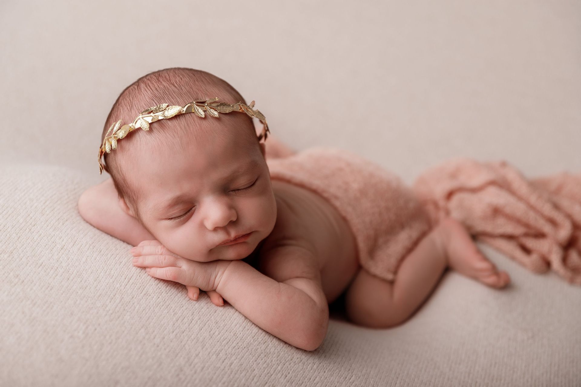 Una niña recién nacida que lleva una diadema dorada está durmiendo sobre una manta.