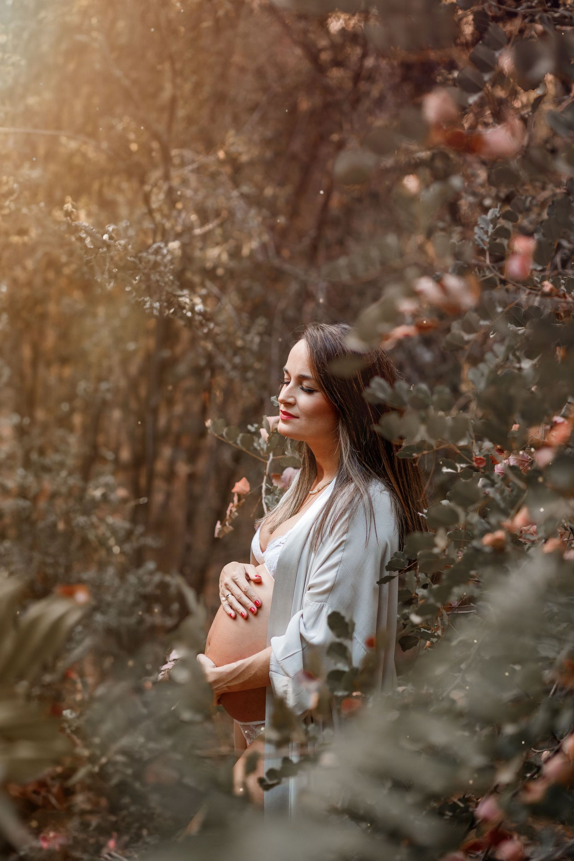 una mujer embarazada está parada en un bosque sosteniendo su barriga.