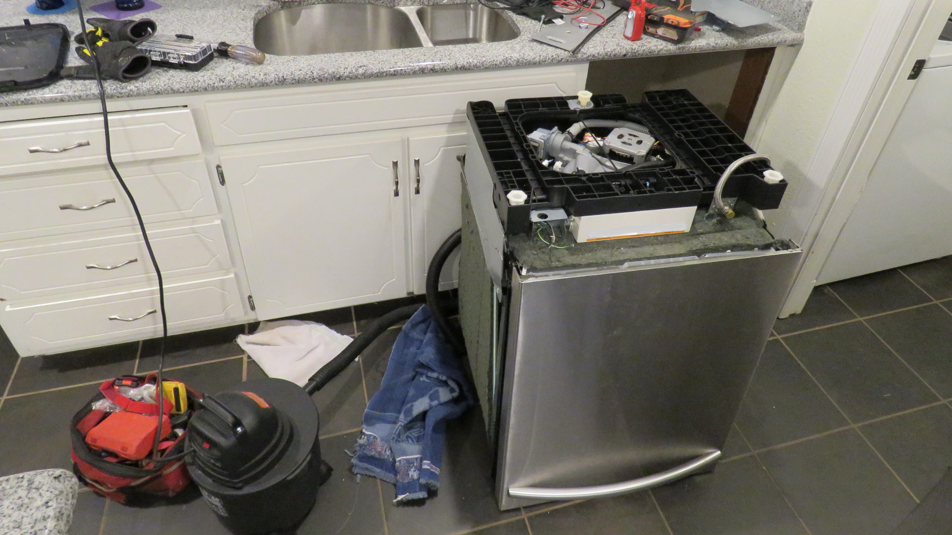 A stainless steel dishwasher is being repaired in a kitchen.
