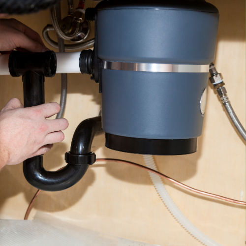 A person is fixing a garbage disposal under a sink