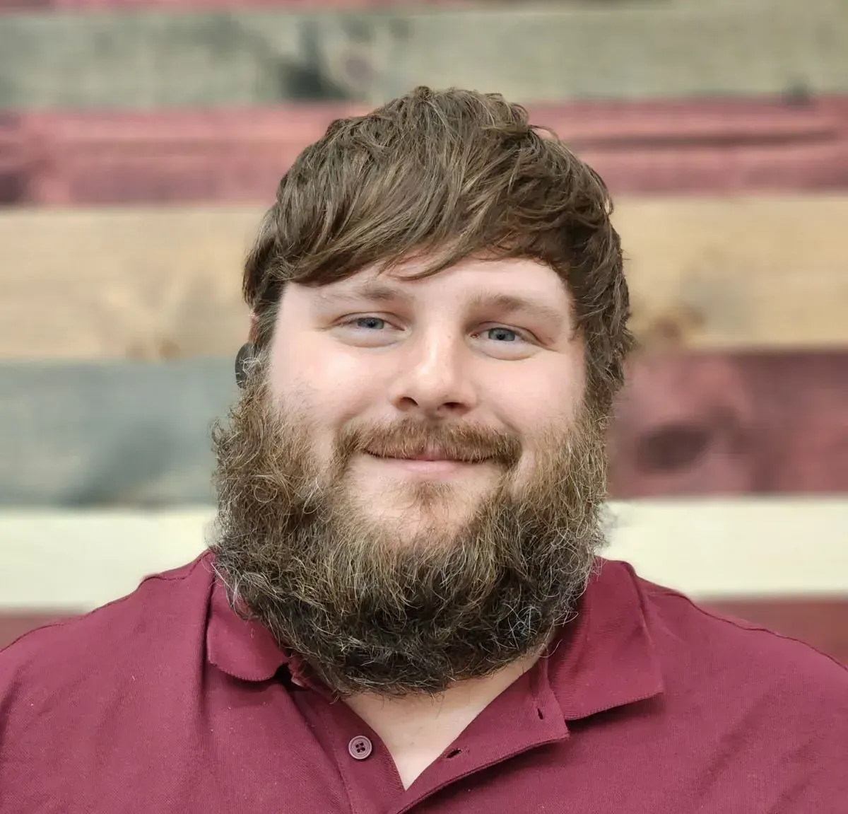 A man with a beard is wearing a red shirt and smiling.