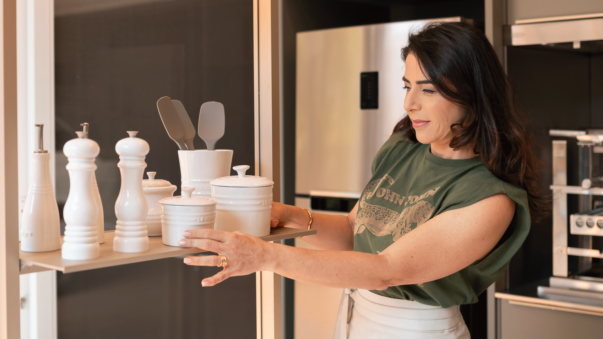 Uma mulher está parada na cozinha segurando uma bandeja com panelas e frigideiras.