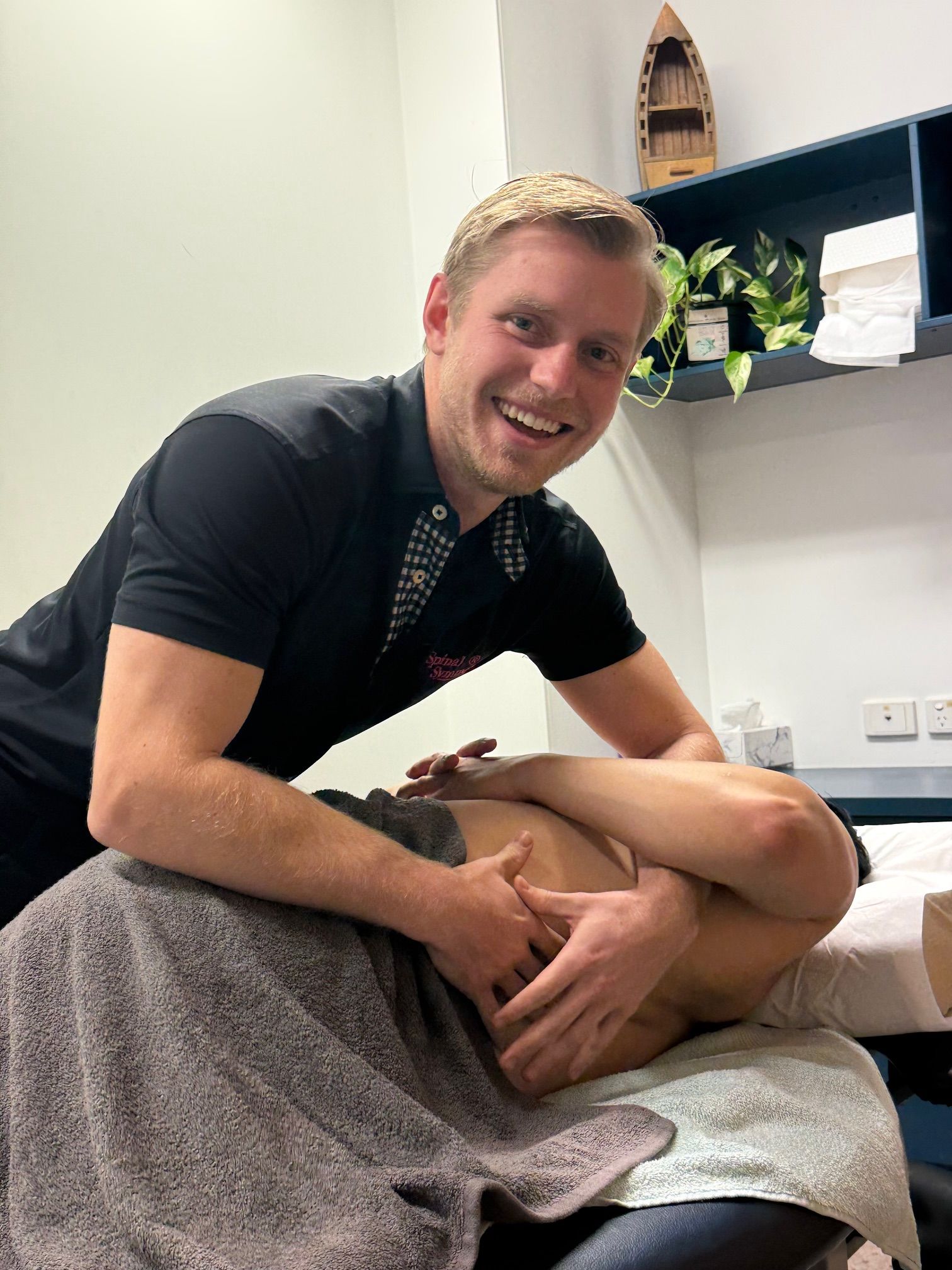 Man giving back massage to a person lying on a massage table. Smiling. Indoors — Spinal Symmetry In Salamander Bay, NSW