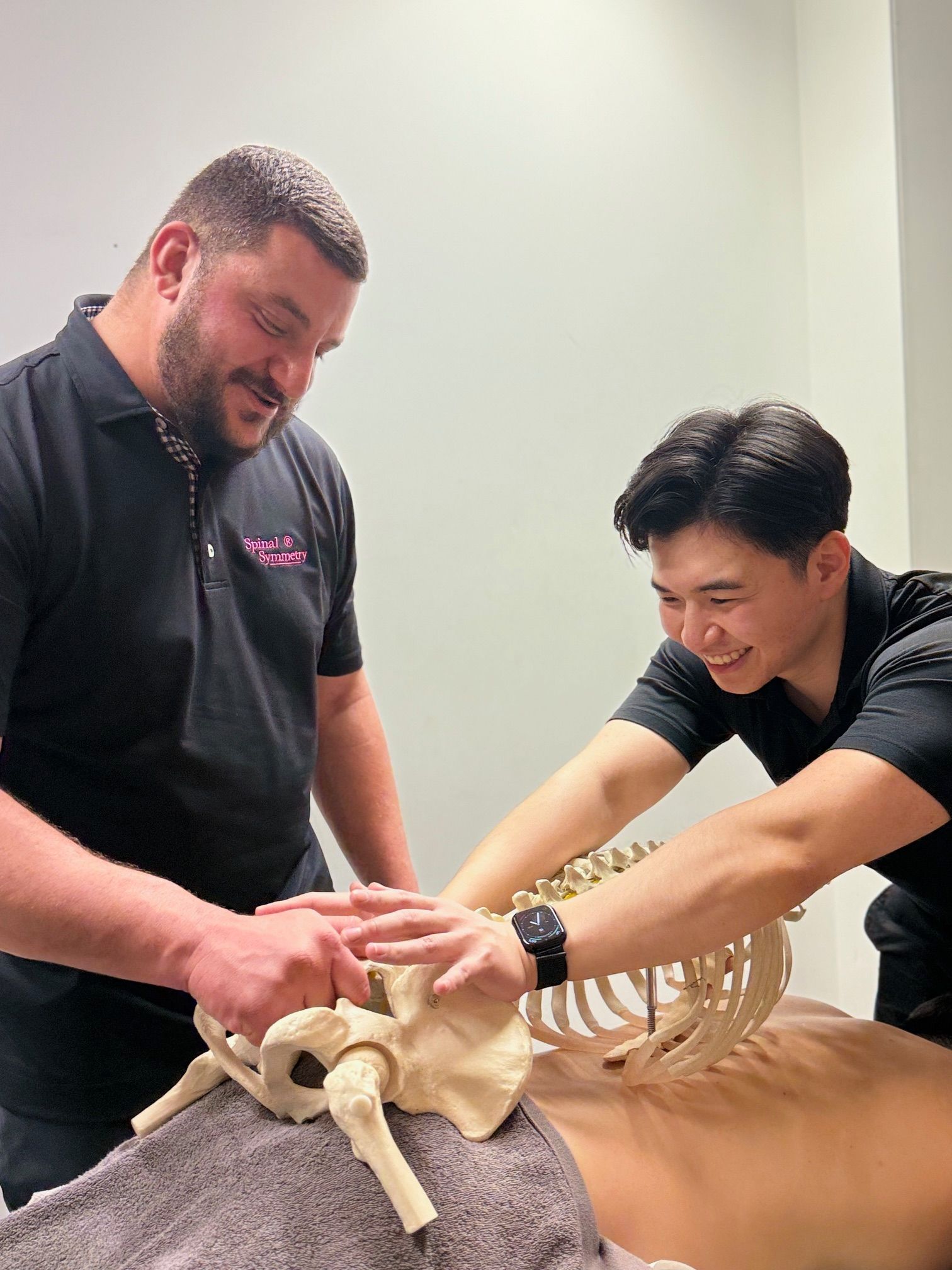 Two Men Examining a Skeleton Model Laid on a Massage Table — Spinal Symmetry In Port Stephens, NSW