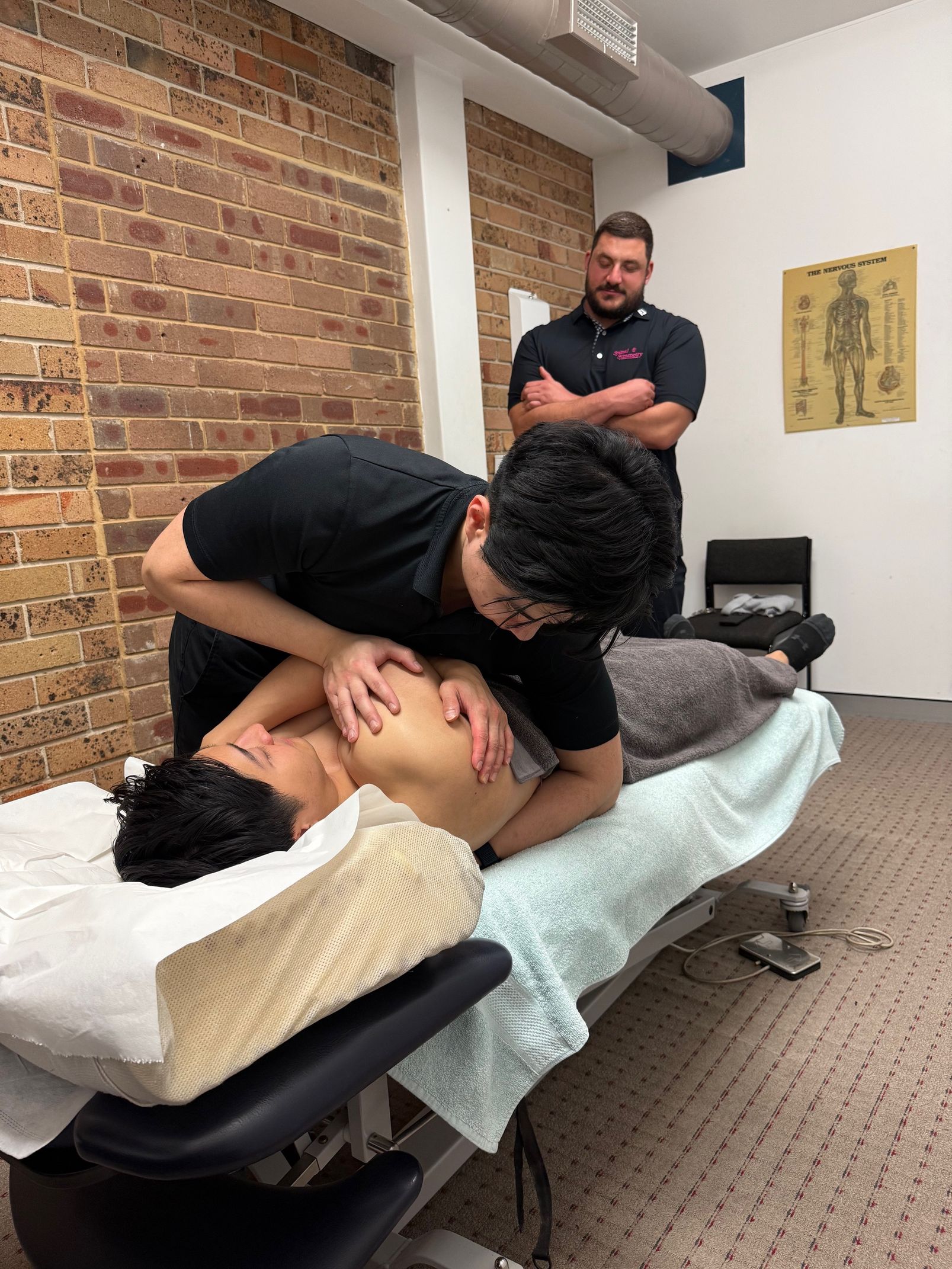 Two Men in a Chiropractic Office: One Adjusting a Patient on a Table — Spinal Symmetry In Port Stephens, NSW