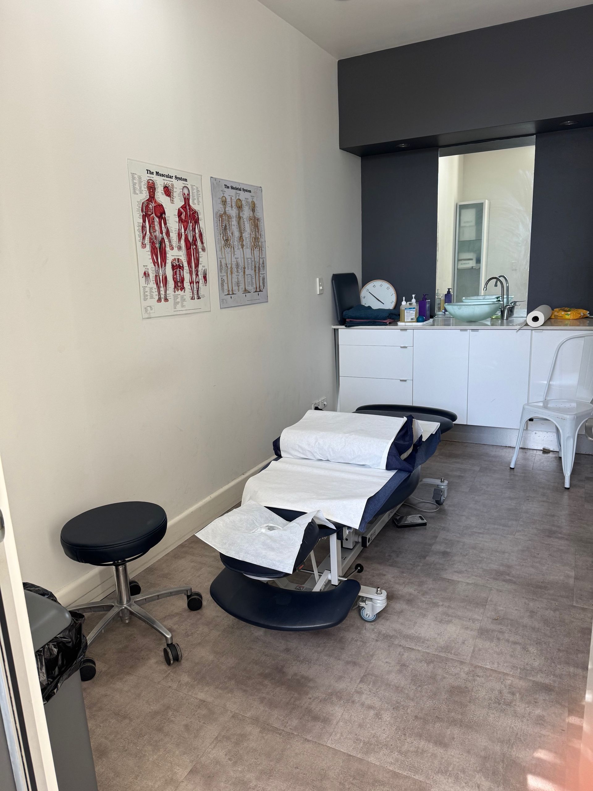 A chiropractic chair is in a room with posters of body and spine diagrams  — Spinal Symmetry In Seaforth, NSW
