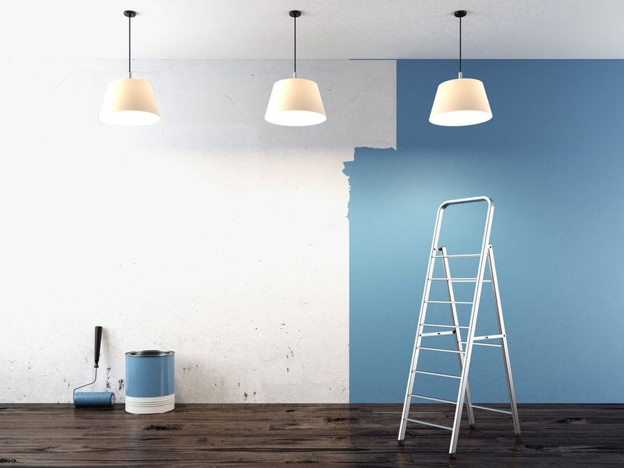 a blue wall half painted white with a ladder and paint tools on the floor with 3 pendant lights hanging from ceiling