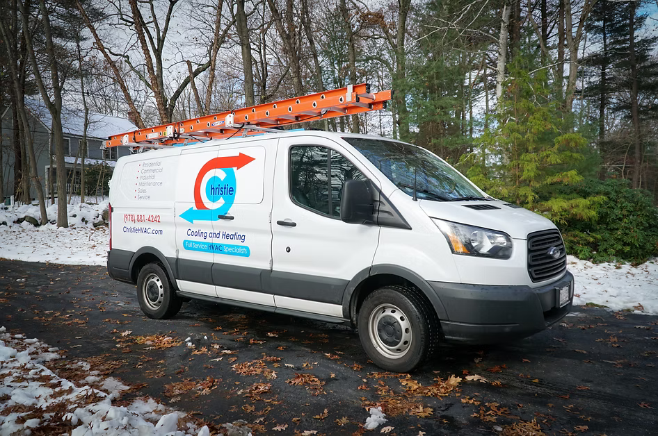 White service van with ladder, logo on side, parked on snowy road.