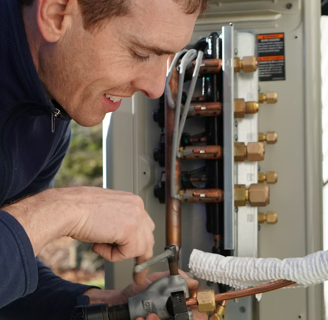 Man working on HVAC unit, outdoors, using a pipe cutter.